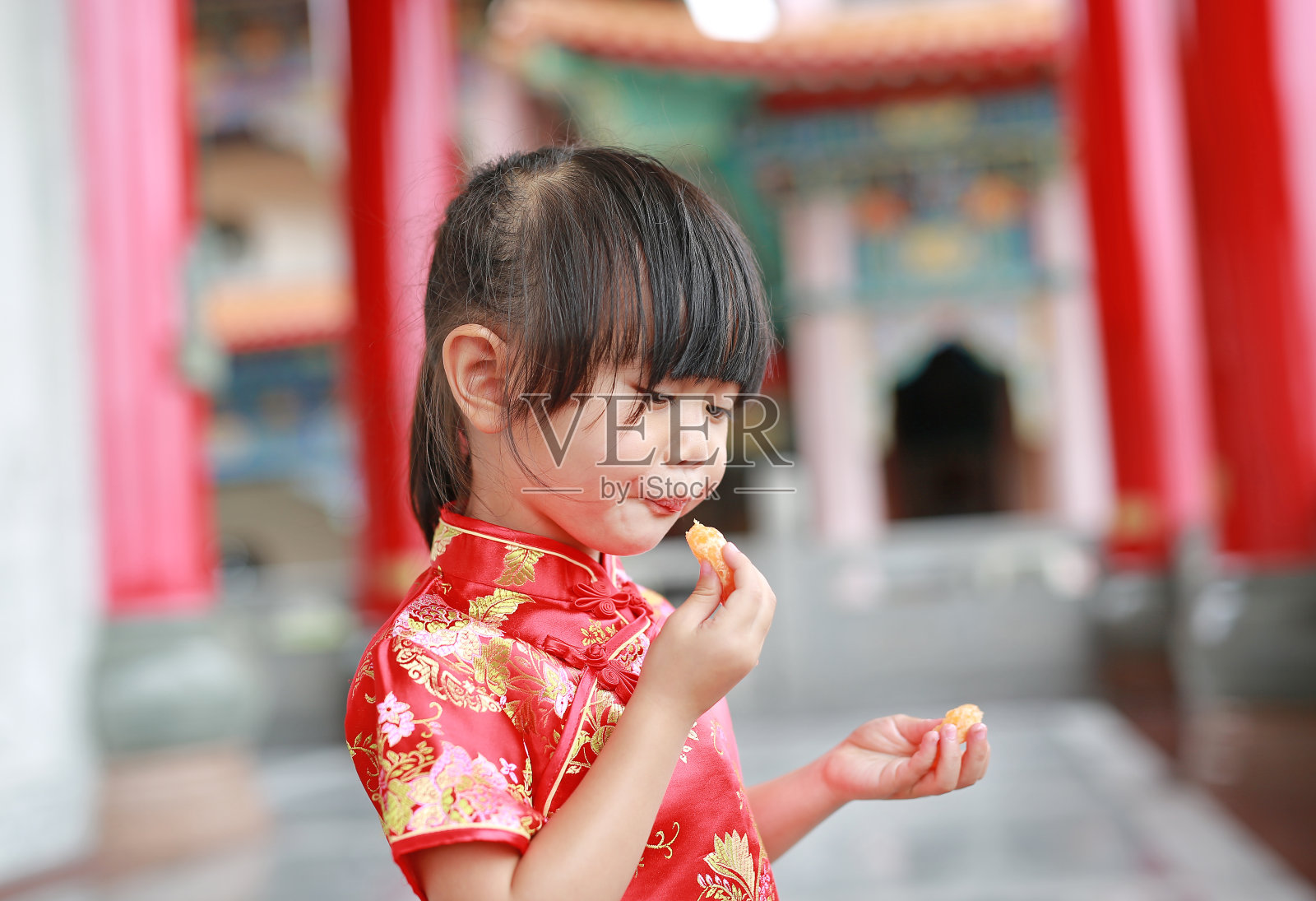 可爱的亚洲小女孩穿着中国传统服饰吃神圣的橘子。照片摄影图片
