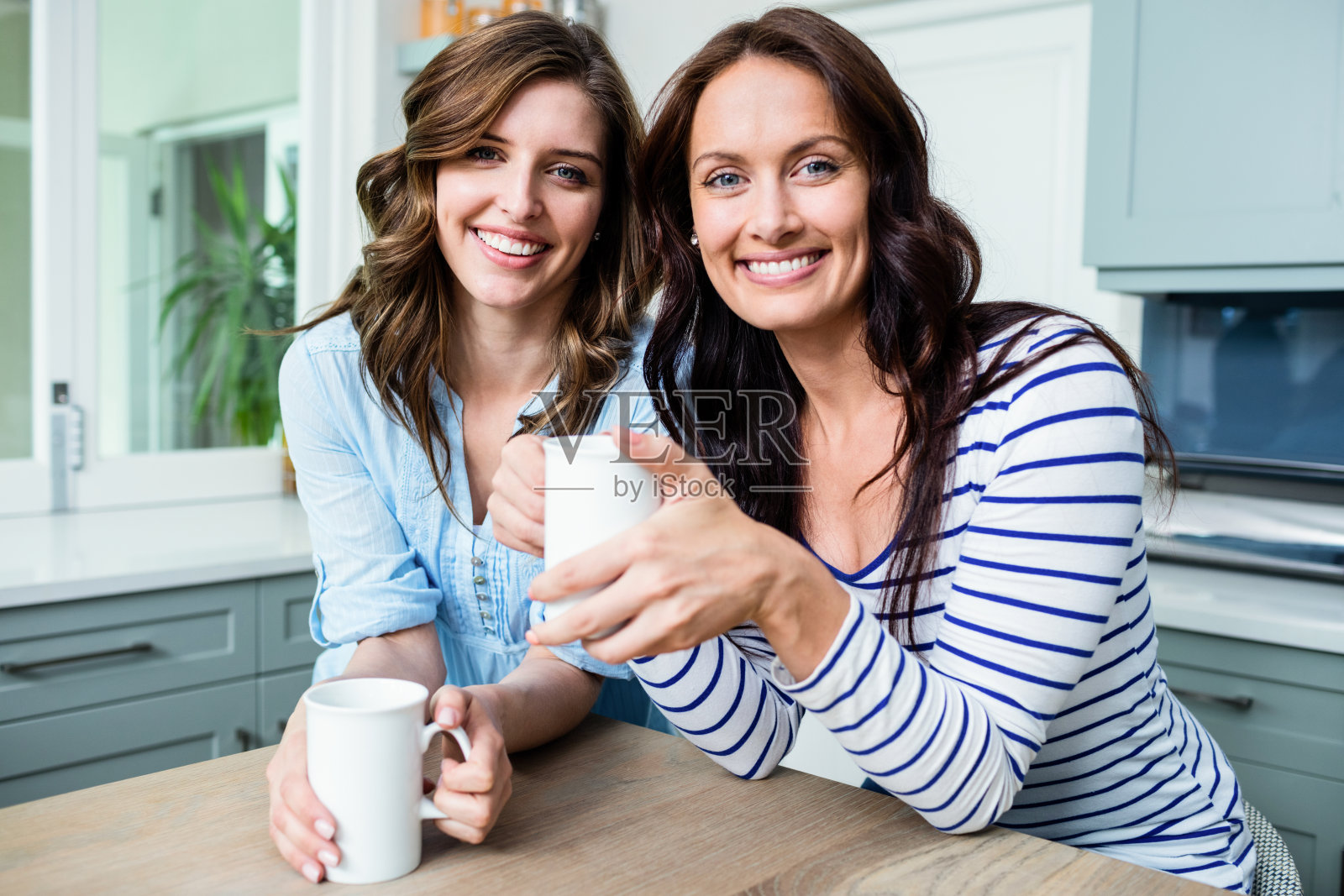 微笑的女性朋友捧着咖啡杯坐在桌子旁的肖像照片摄影图片