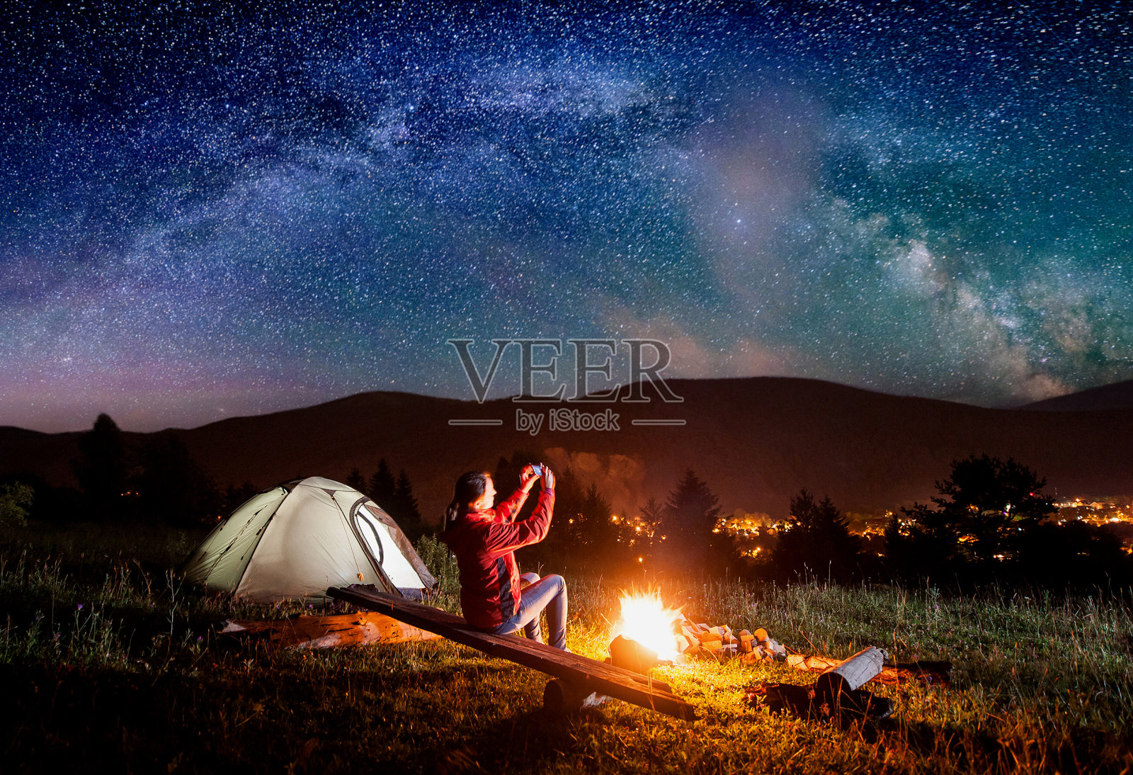 一名徒步旅行者坐在帐篷附近篝火旁的木板上，用手机拍下了令人难以置信的星空与银河的照片照片摄影图片