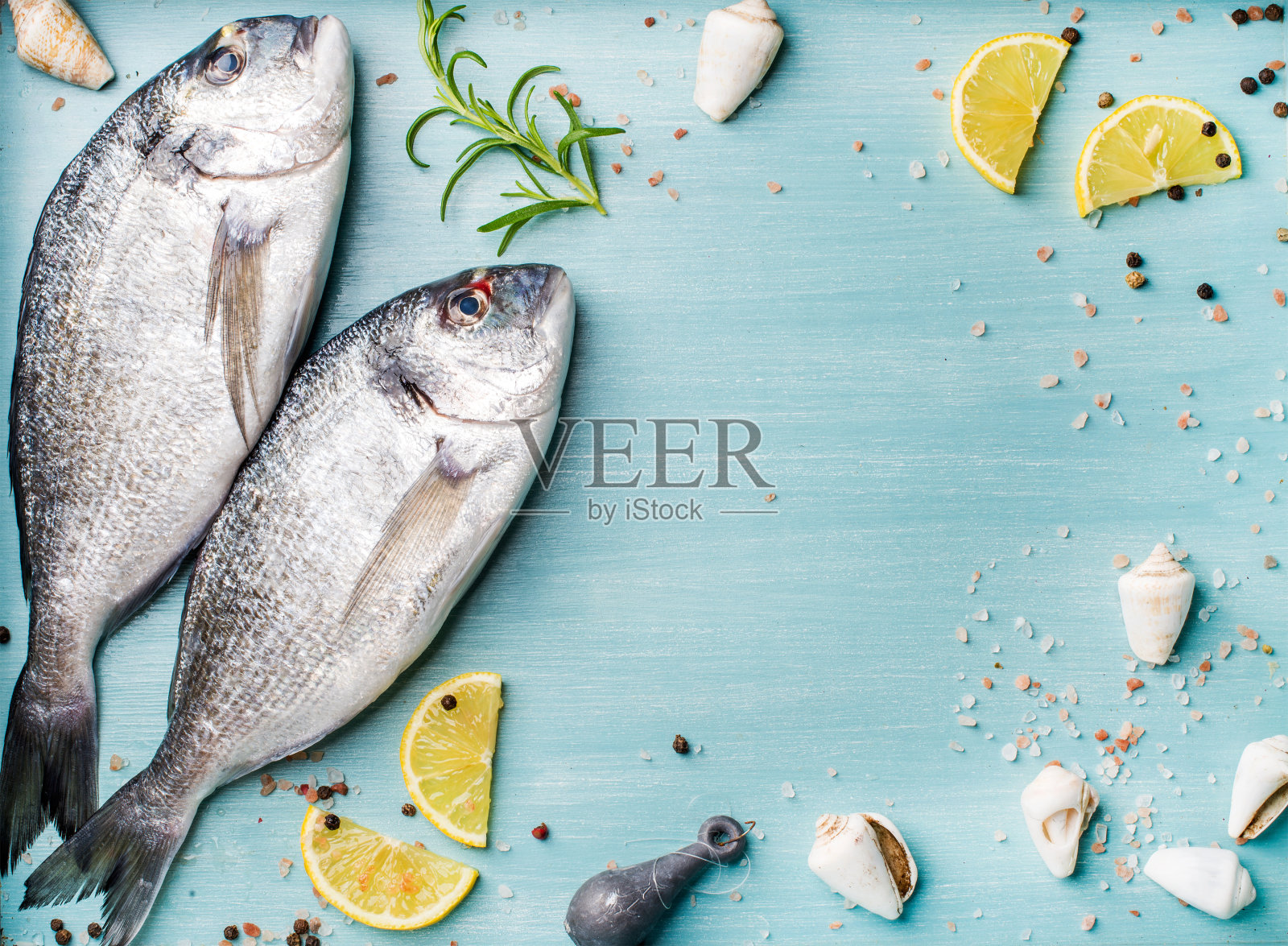 新鲜的生海鲷鱼装饰柠檬片，香草和贝壳在蓝色的木制背景，复制空间照片摄影图片