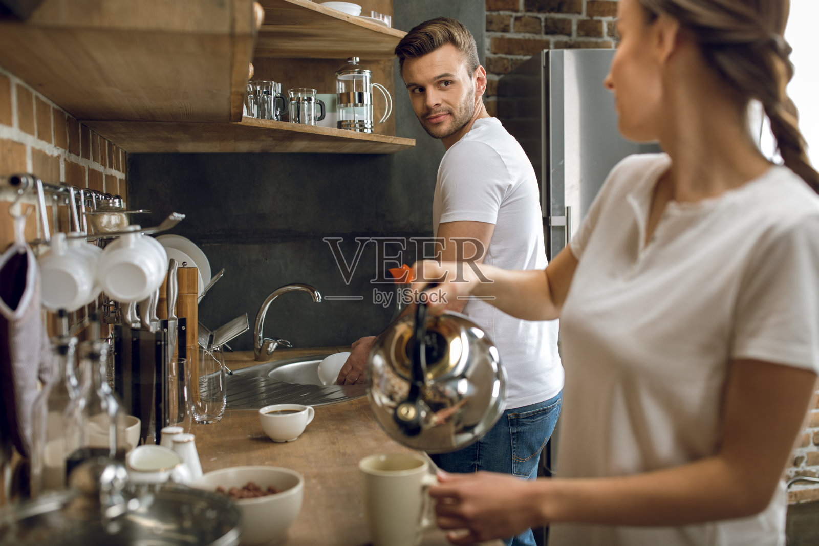 女人往杯子里倒咖啡，男人洗碗照片摄影图片