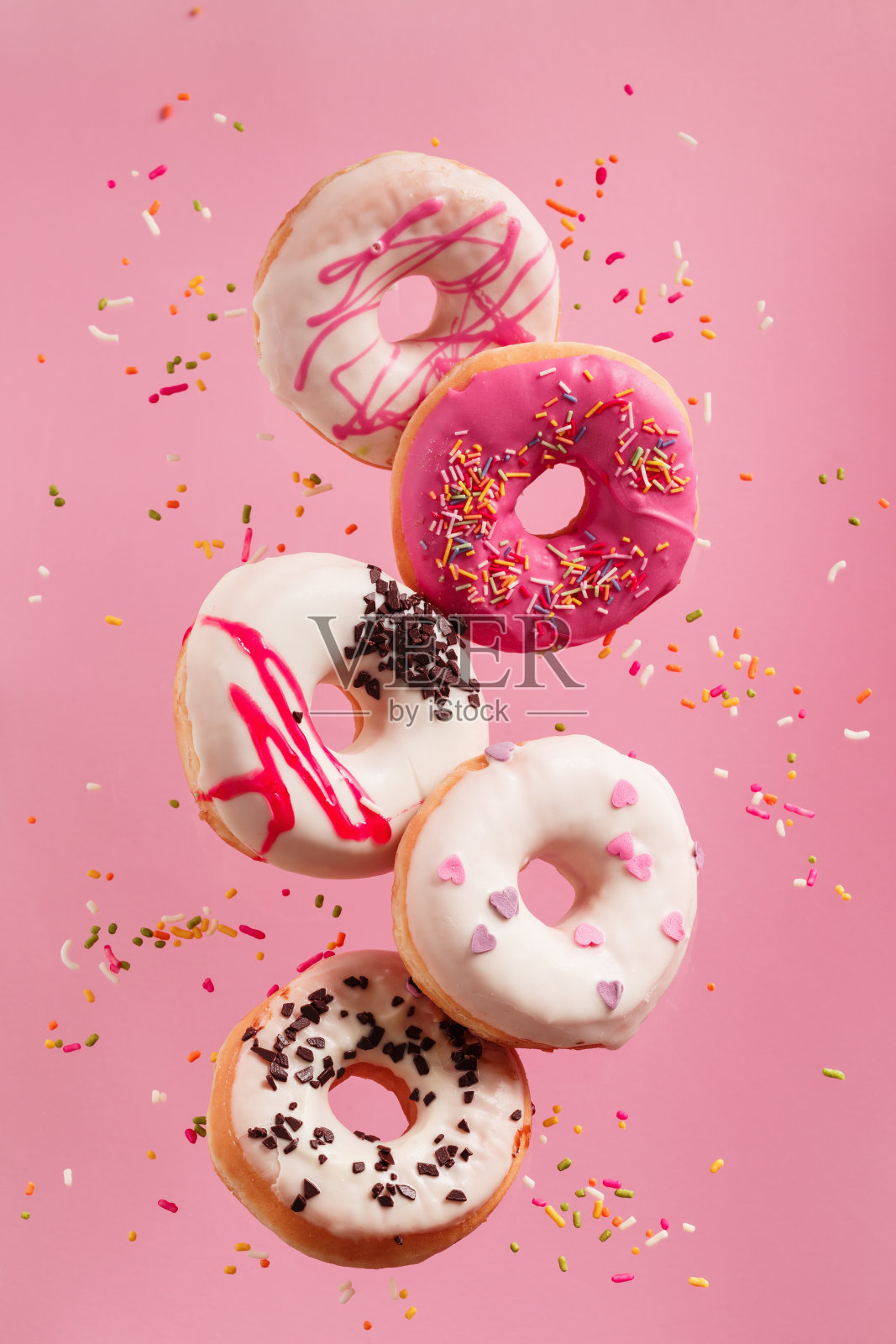 各种装饰甜甜圈的运动落在粉红色的背景。照片摄影图片