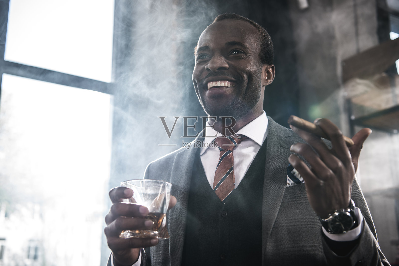 微笑的非裔美国商人拿着威士忌和抽雪茄的杯子照片摄影图片