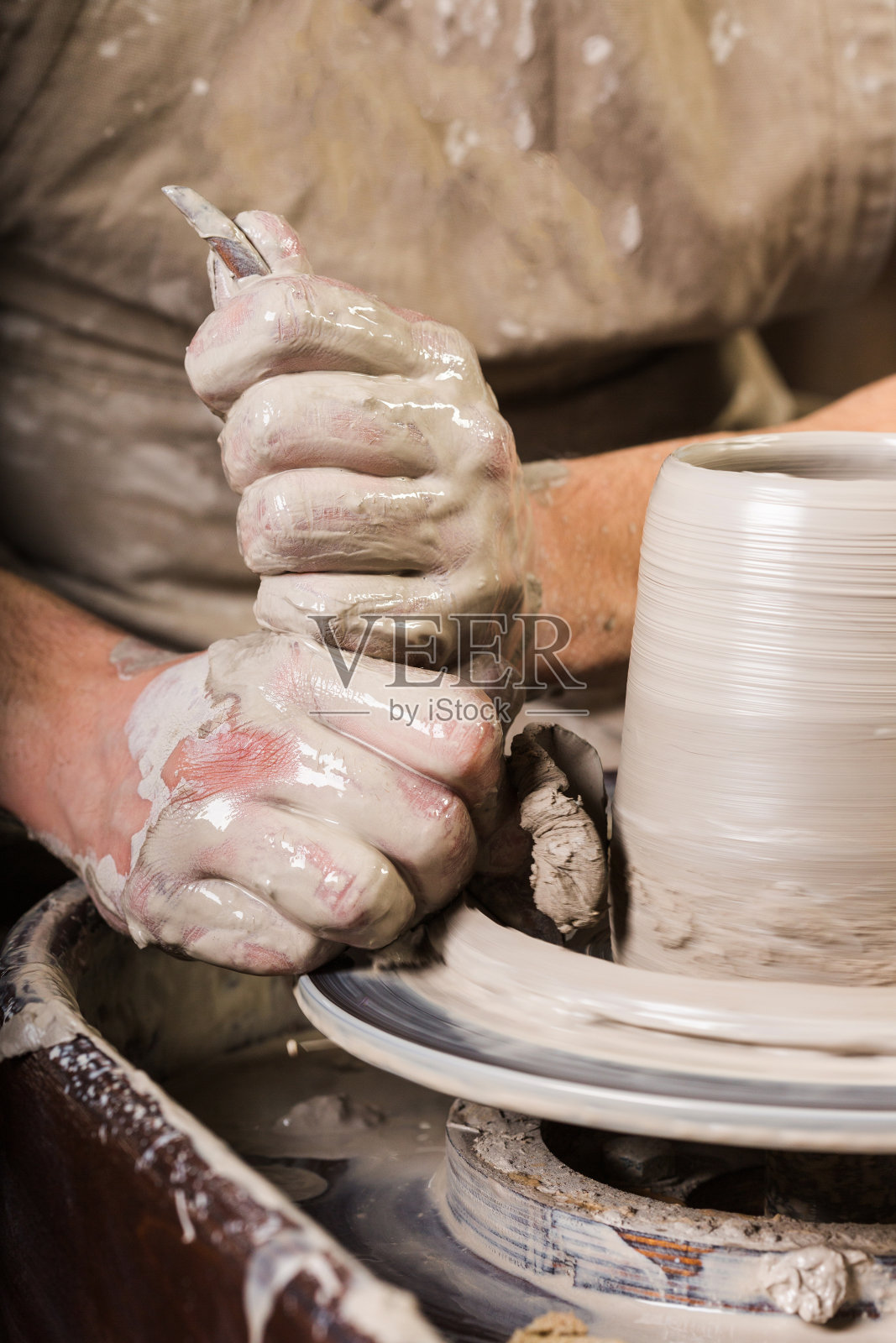 陶艺、工坊、陶艺艺术概念——男性大师用海绵和雕刻工具雕刻器具，男子双手用陶工的轮子，手指形成生泥的形状，垂直照片摄影图片