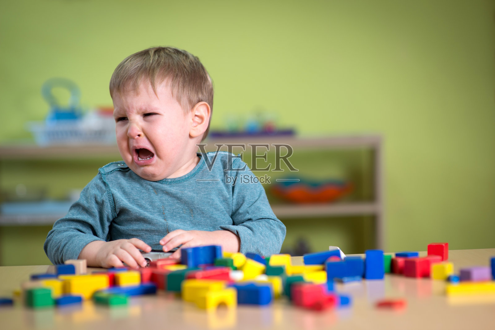 带着蒙特梭利玩具在托儿所的泪流满面的男孩照片摄影图片