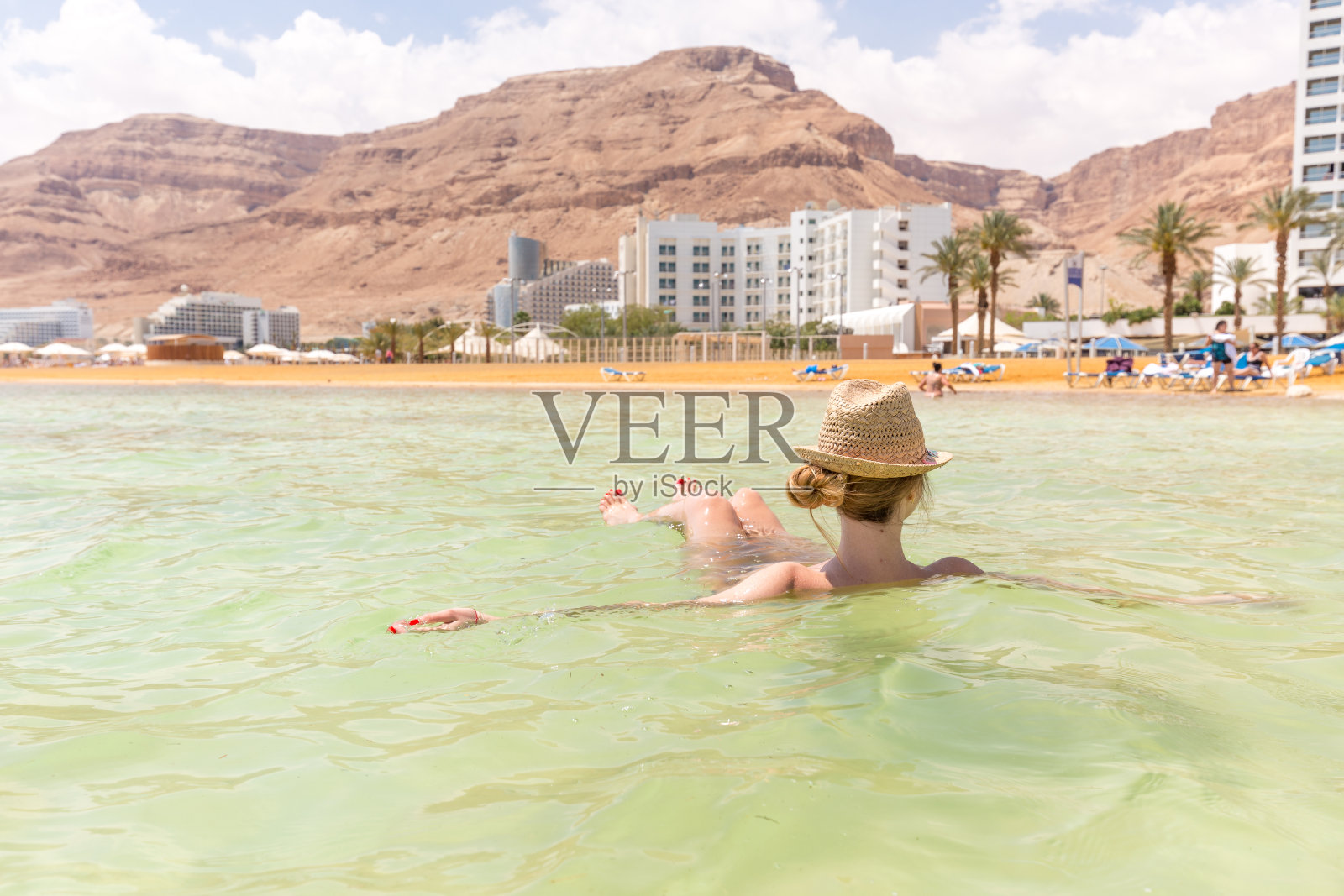 年轻女子在死海的咸水里游泳。照片摄影图片