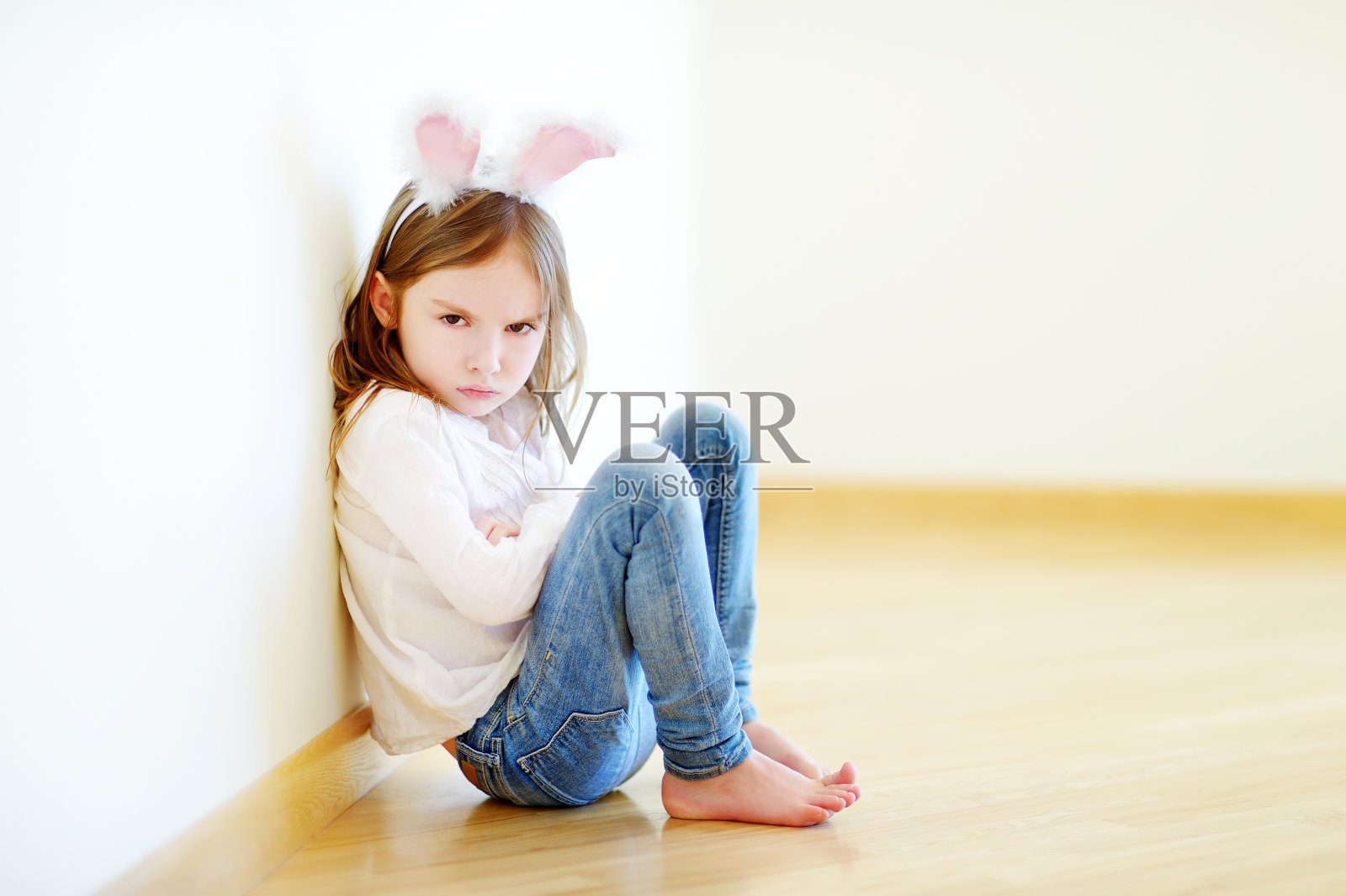 非常生气的小女孩戴着兔耳朵坐在地板上照片摄影图片