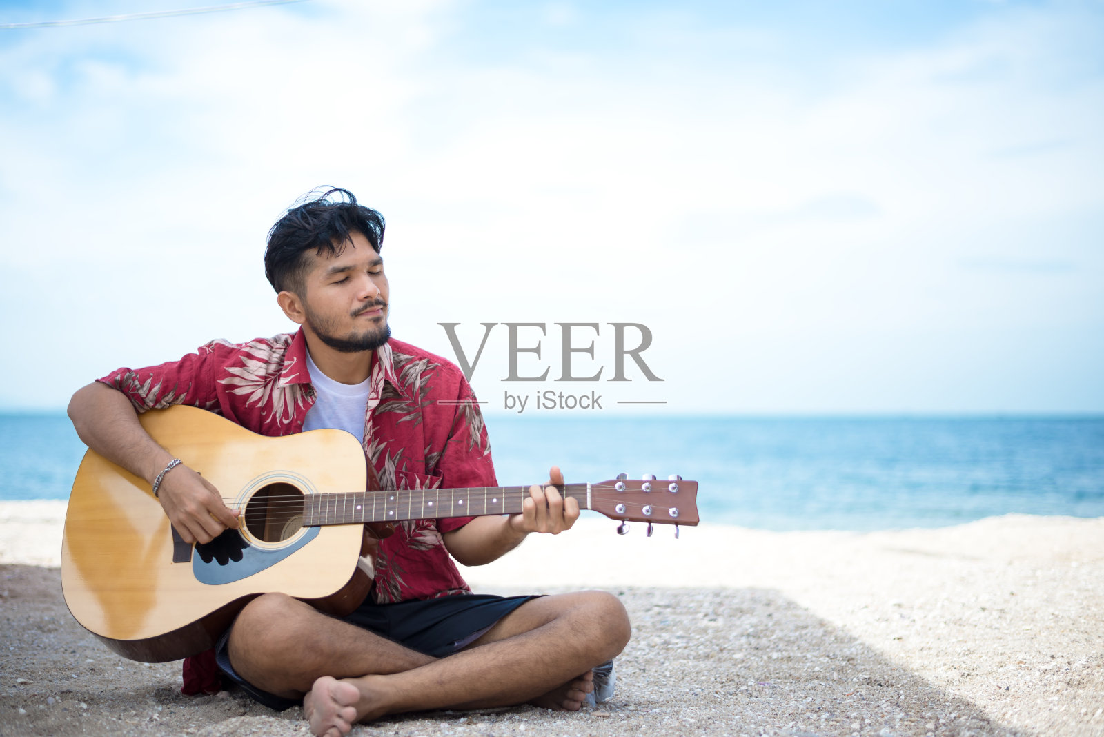度假时坐在海滩上弹古典吉他的帅哥照片摄影图片