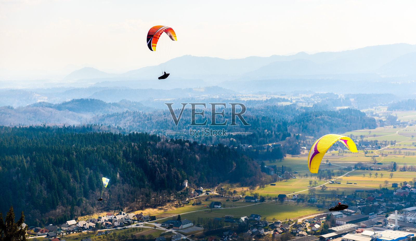 三个滑翔伞正在山谷中飞行。照片摄影图片