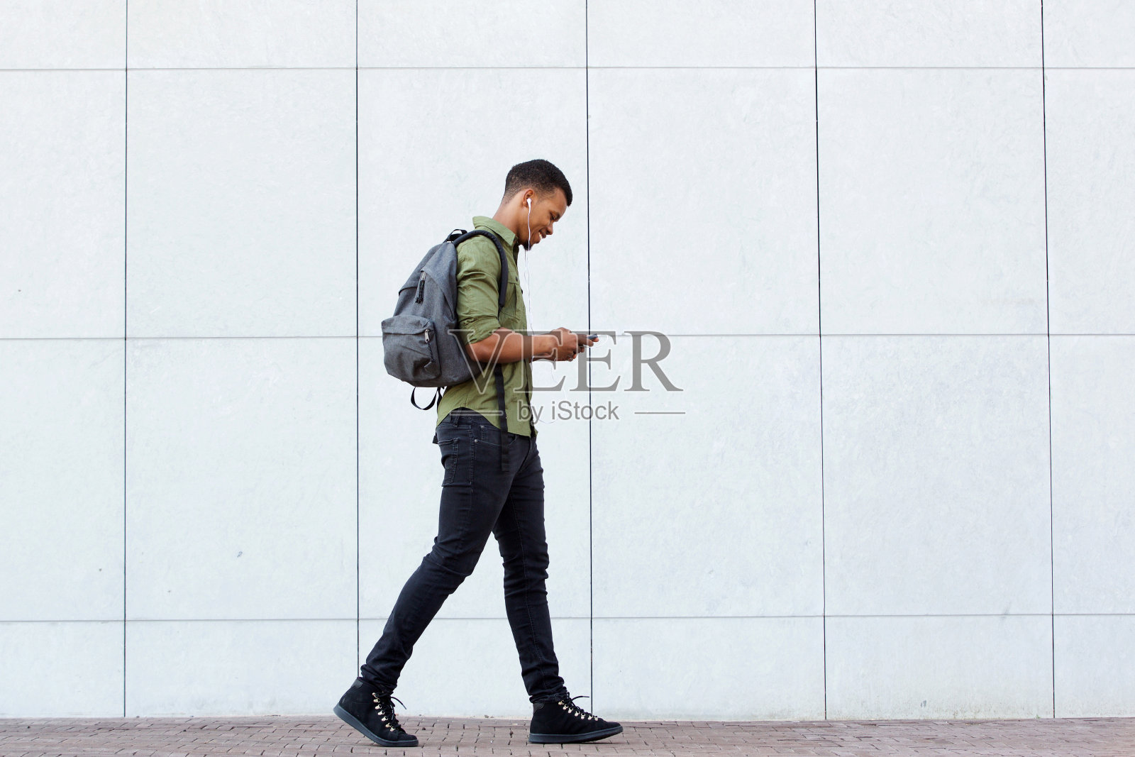 微笑的男人背着背包走路智能手机和耳机照片摄影图片