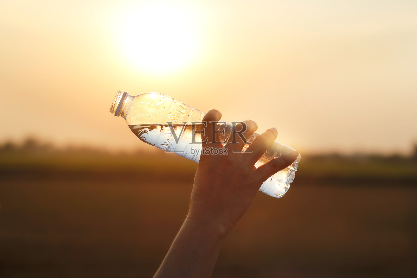 手握饮用水在日落的背景照片摄影图片