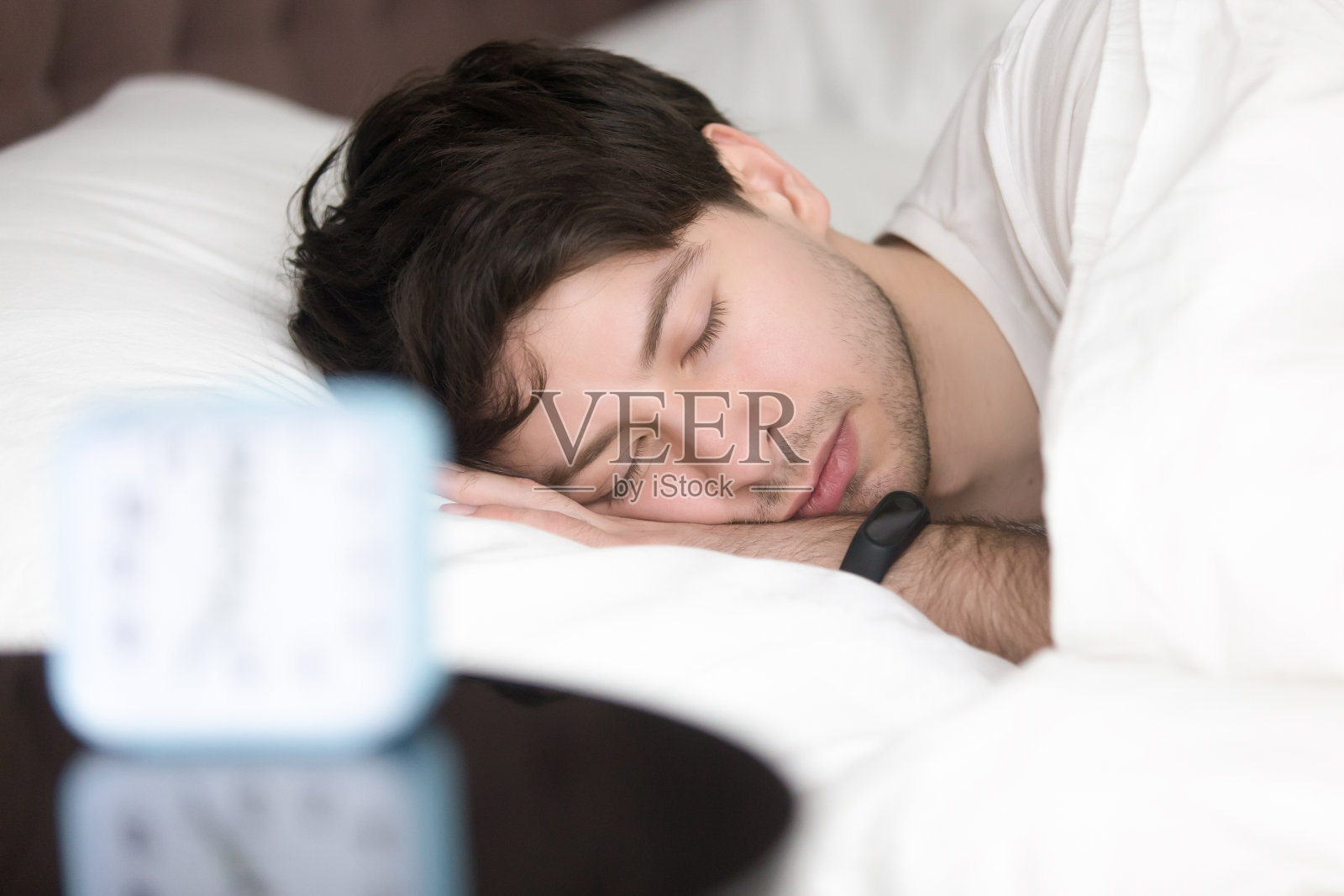 一个年轻人戴着智能腕带睡在闹钟旁边照片摄影图片