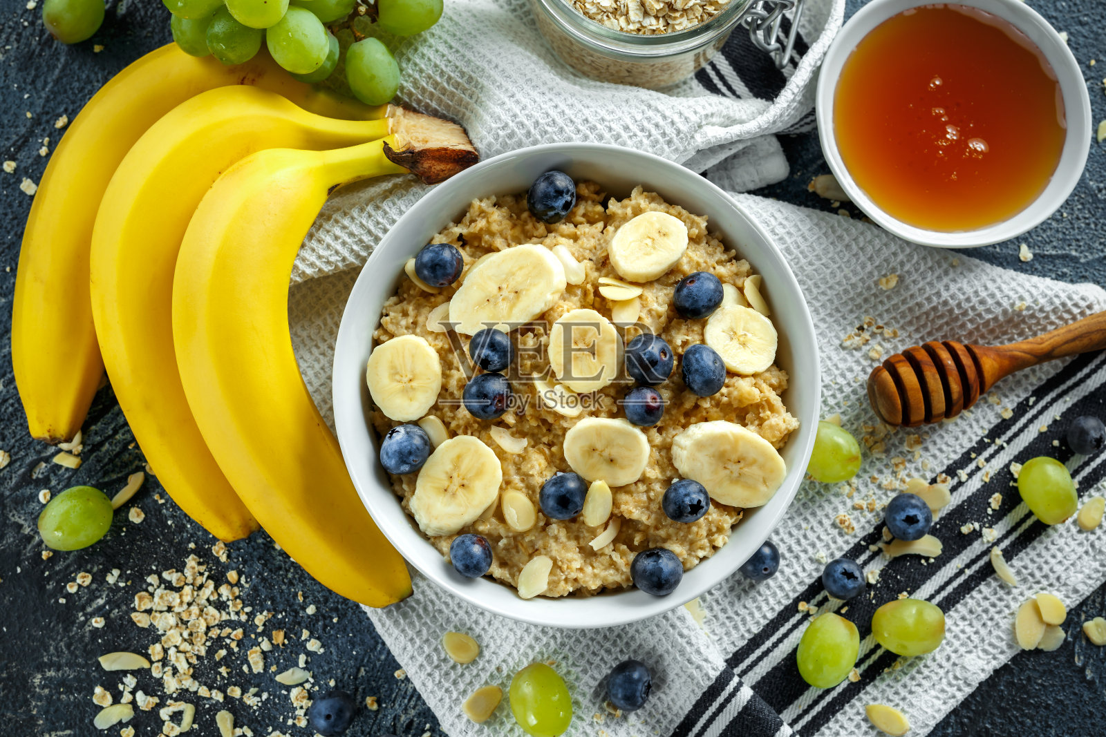 一碗健康的早餐燕麦粥，里面有成熟的蓝莓、香蕉、蜂蜜、杏仁和绿葡萄。俯视图照片摄影图片