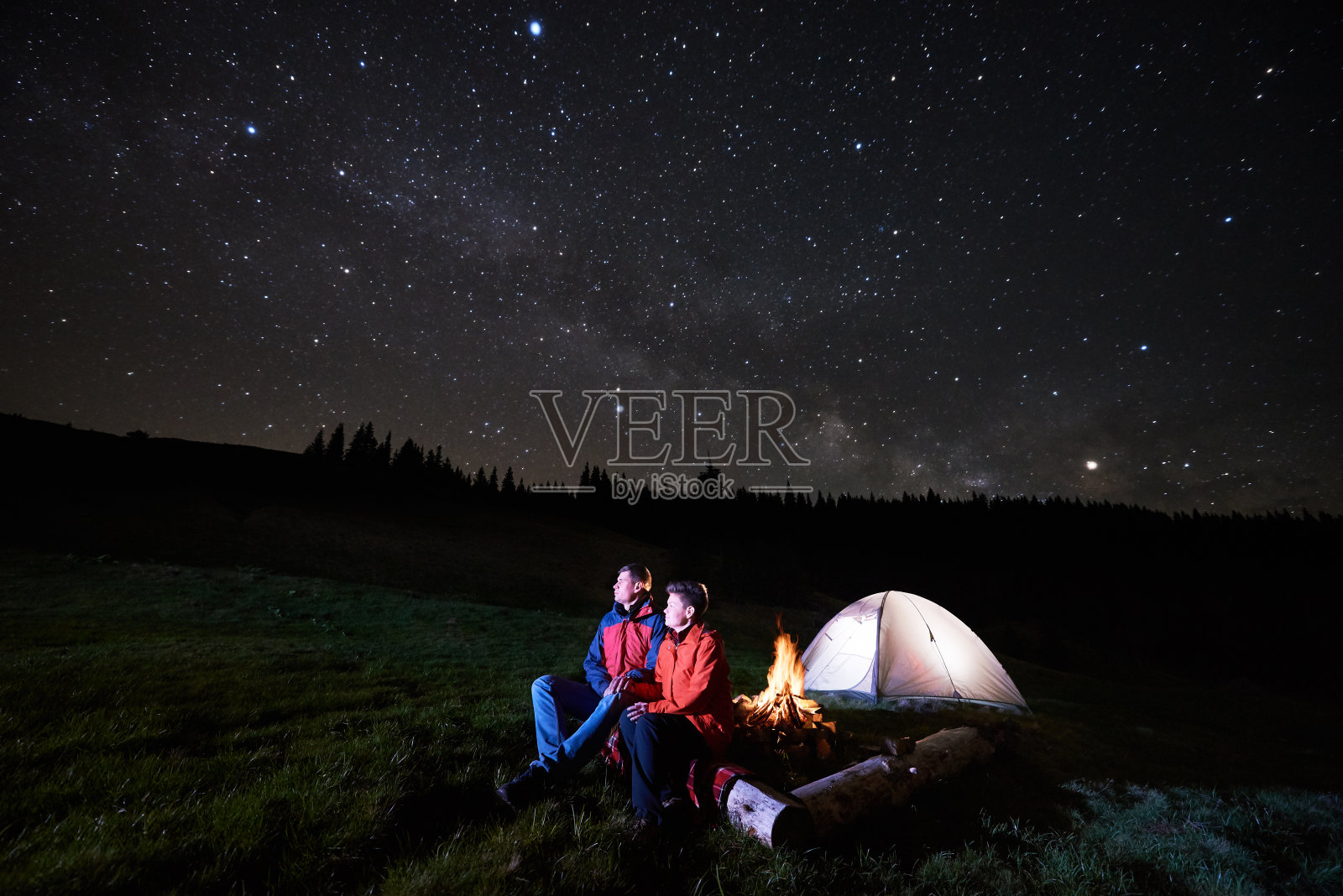 晚上露营。在星空下，男男女女游客在明亮的帐篷旁的篝火旁休息。低光照片摄影图片