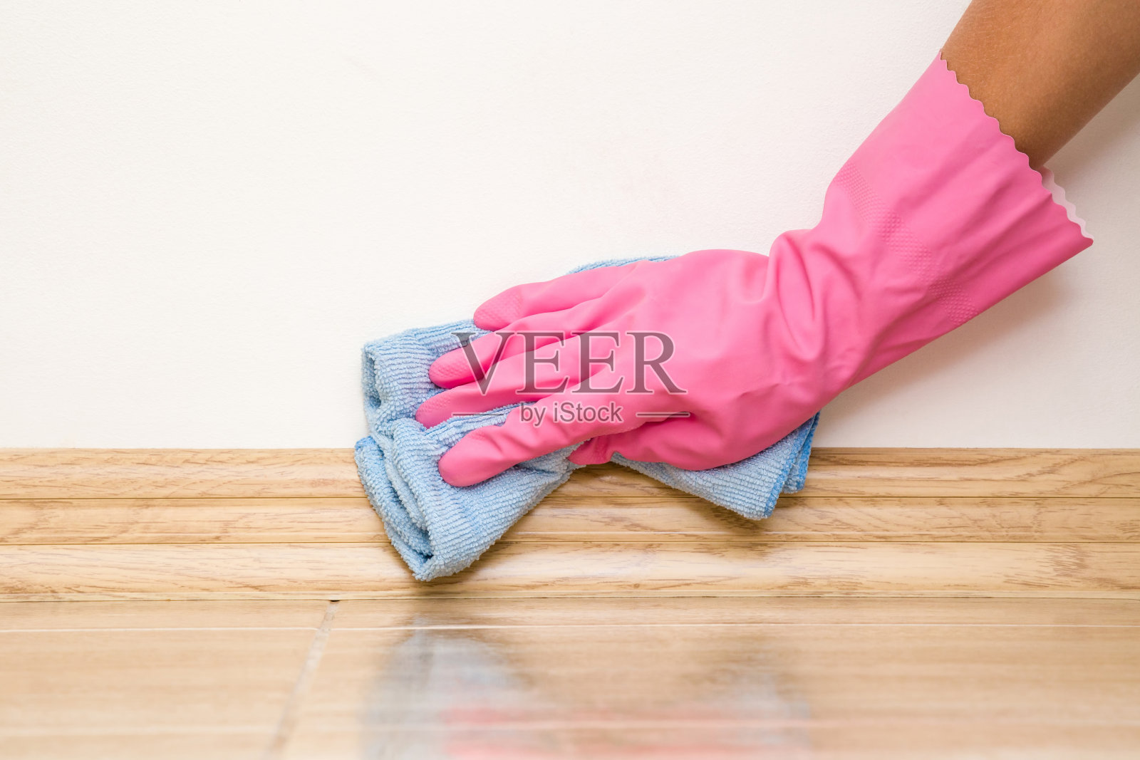 手戴橡胶防护手套，用抹布擦拭地板脚板上的灰尘。早春大扫除或定期大扫除。女保洁员打扫房子。照片摄影图片