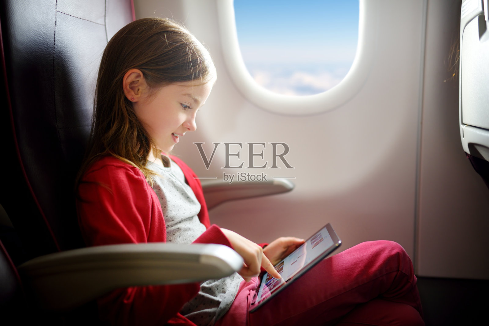 可爱的小女孩乘飞机旅行。儿童坐在飞机窗口，使用数字平板电脑照片摄影图片