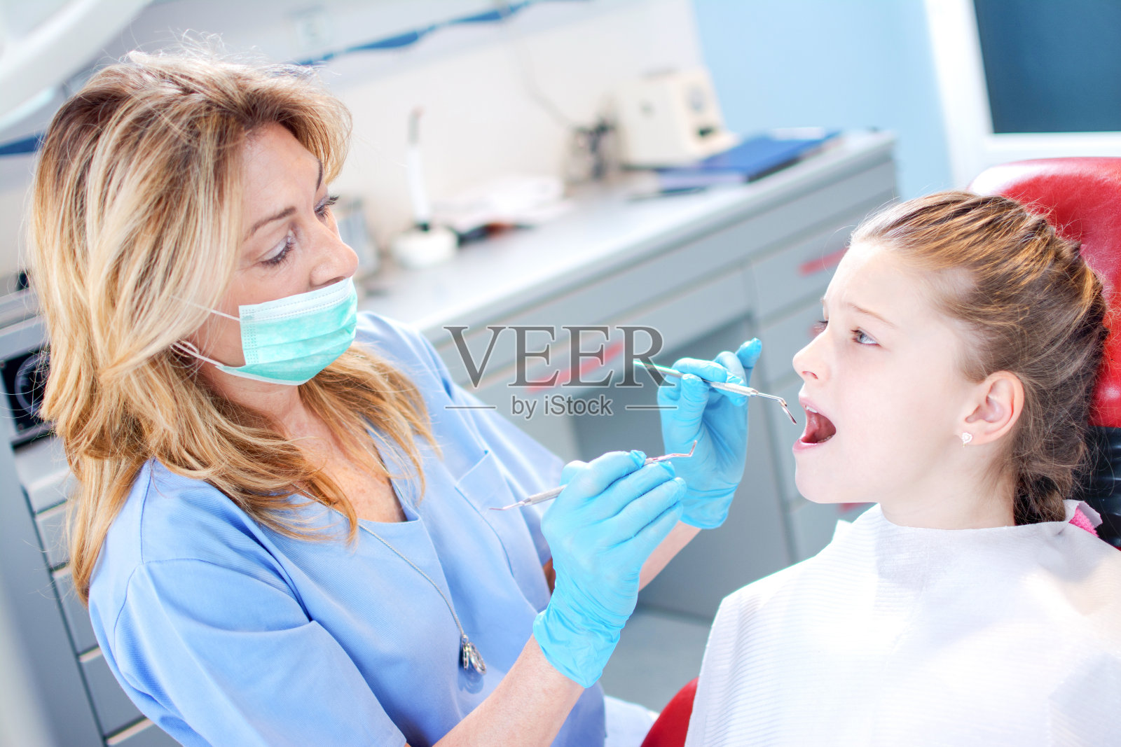 年轻的女孩正在牙科诊所接受专业女牙医的牙齿检查。照片摄影图片