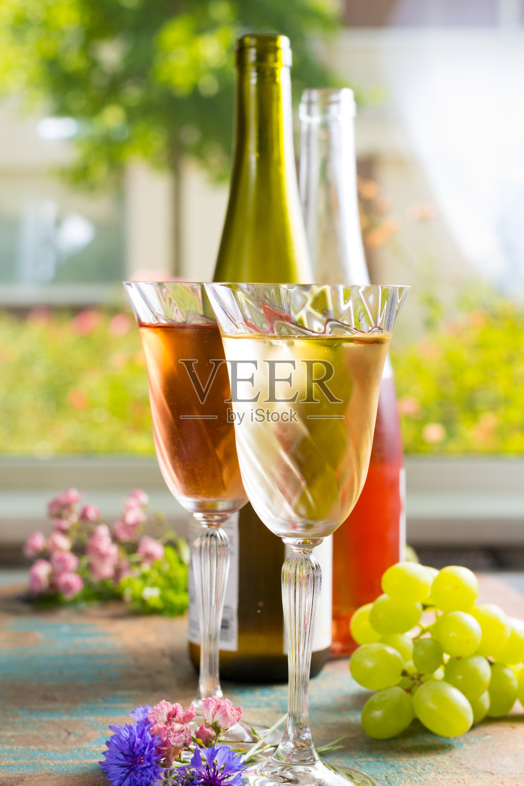 寒冷的夏季葡萄酒，白色和玫瑰色，在新鲜的空气，户外的绿色花园鲜花，阳光明媚的日子里，用漂亮的玻璃杯盛着照片摄影图片