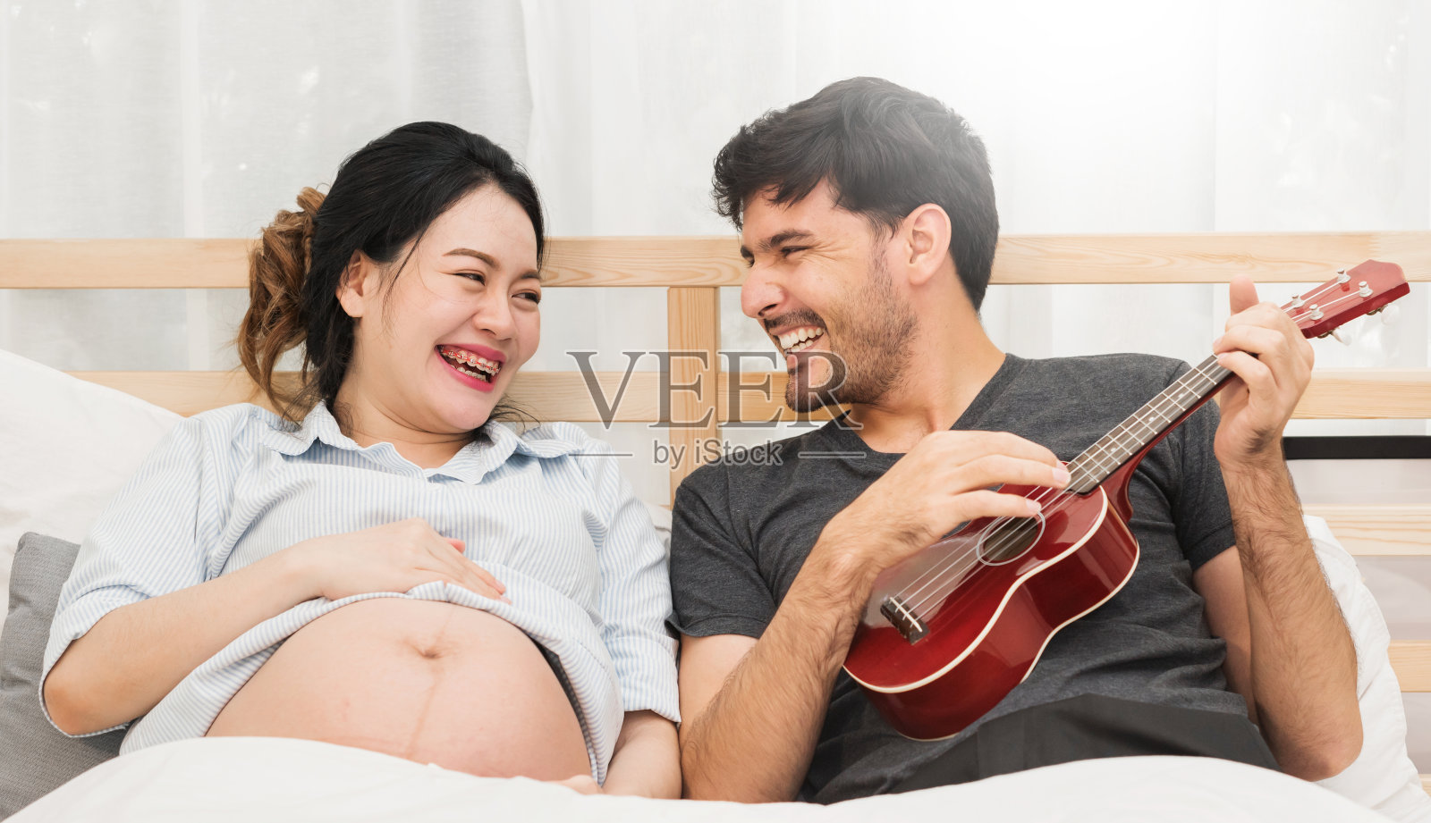 孕妇和丈夫正在弹原声吉他。照片摄影图片