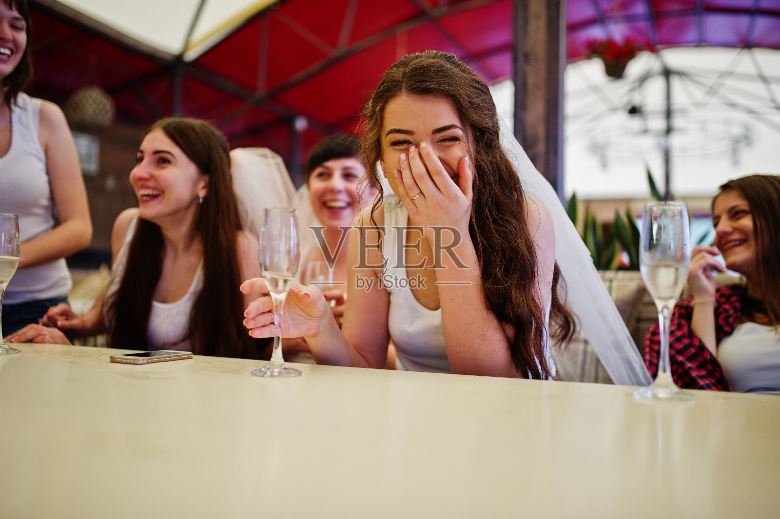 一群穿着白衬衫的快乐女孩坐在桌旁，在女性聚会上喝香槟。照片摄影图片