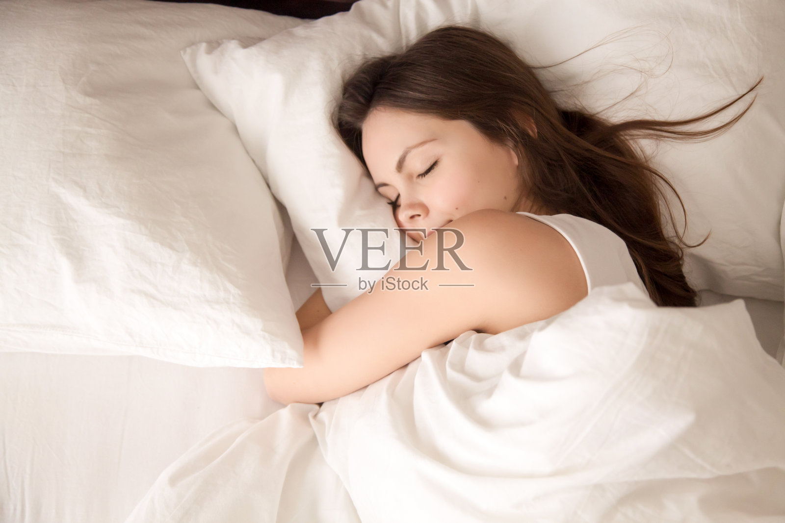 抱着柔软的白色枕头睡在床上的女人照片摄影图片