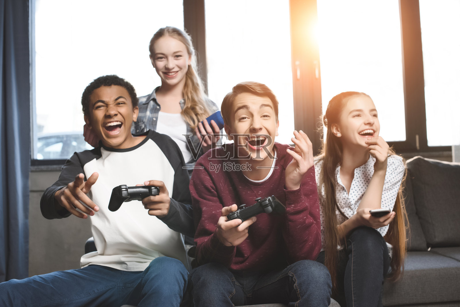 快乐的多文化青少年玩电子游戏与操纵杆在家里，青少年有乐趣的概念照片摄影图片