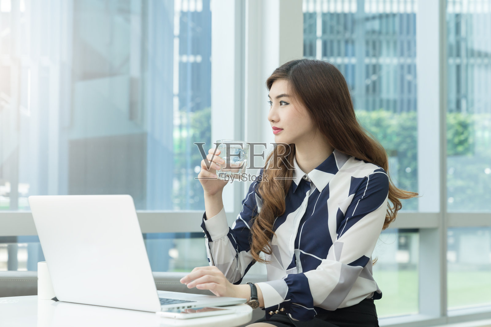 可爱的亚洲女人在现代办公室喝水。职业女性从工作中放松。照片摄影图片