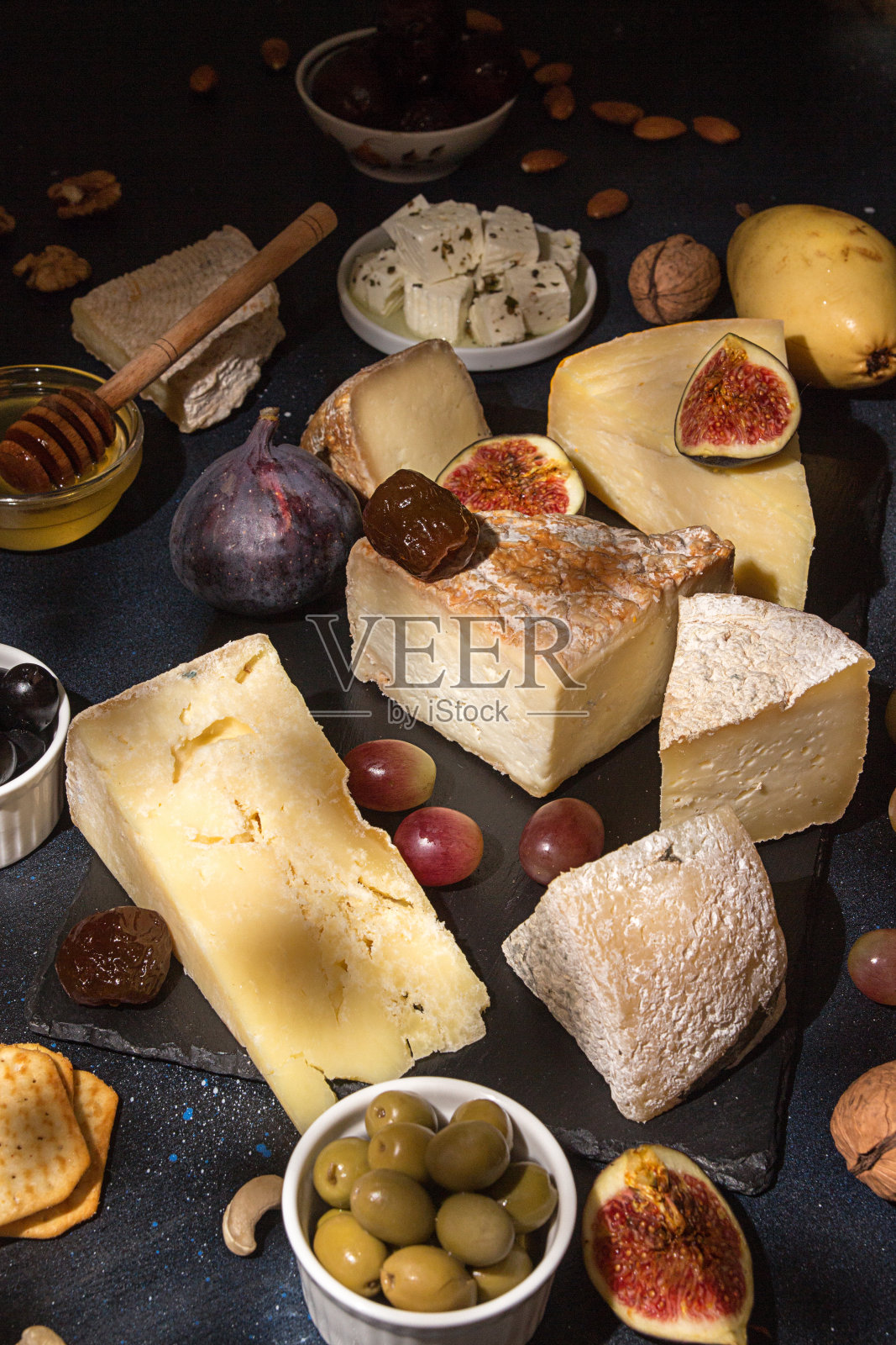 食物成分:发霉的奶酪块，腌李子，蜂蜜，葡萄串，橄榄，无花果，饼干，无花果在黑色背景。照片摄影图片