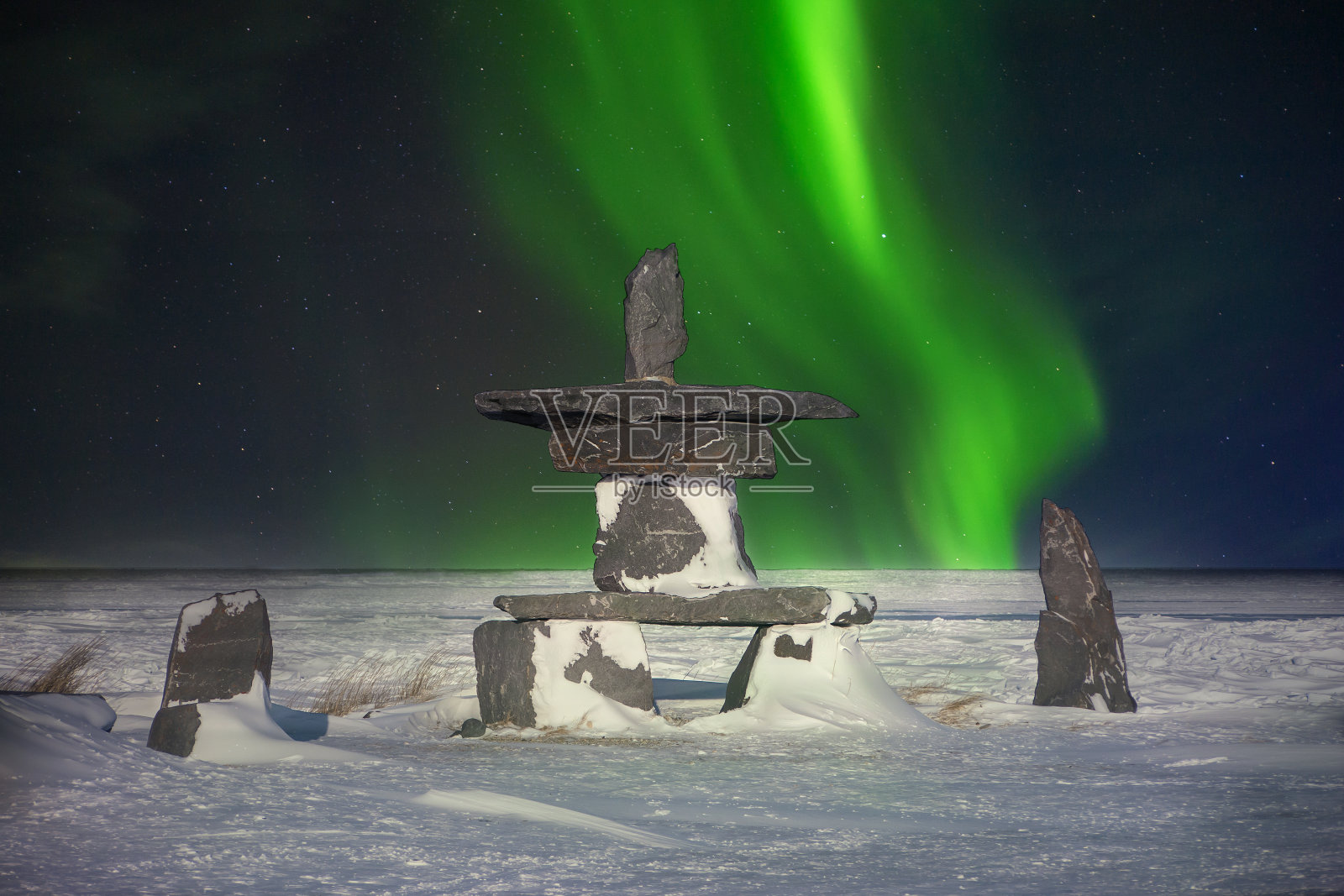 一种传统的石inukshuk，一种因纽特人的文化符号，被用作在遥远的北方指引旅行者的地标，表明他们走在正确的道路上。绿色的北极光在夜空中闪烁。照片摄影图片