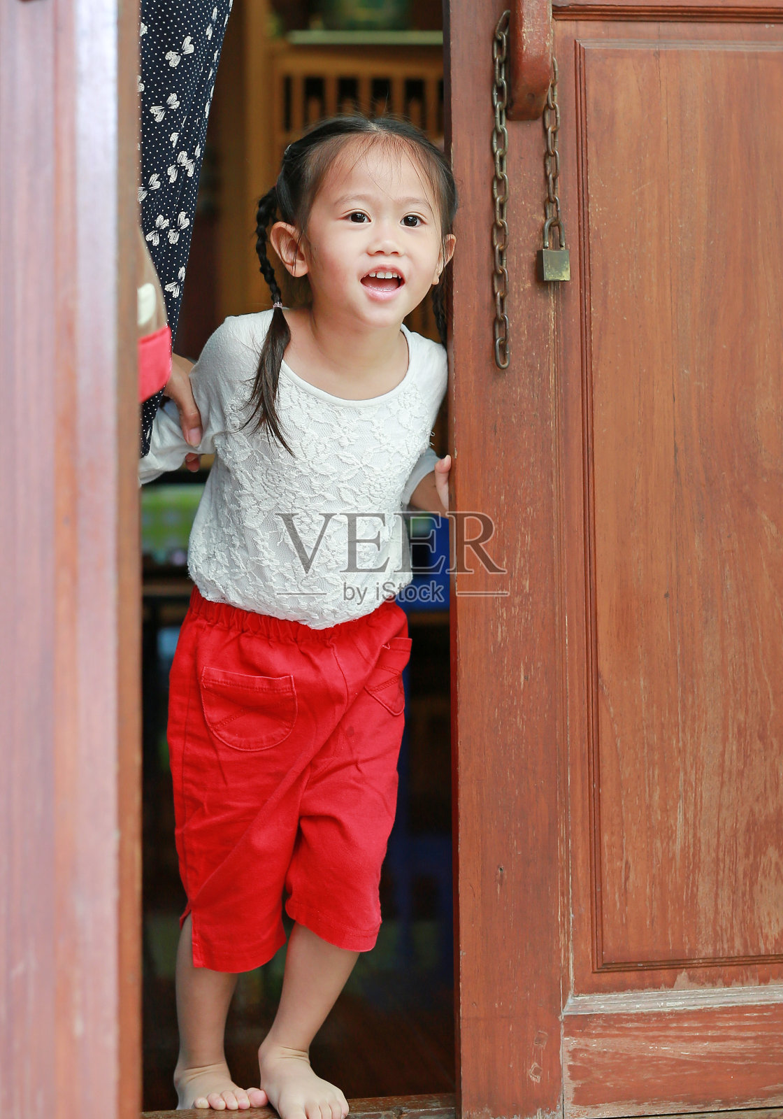 快乐的小女孩笑着玩，打开木屋的门往外看。照片摄影图片