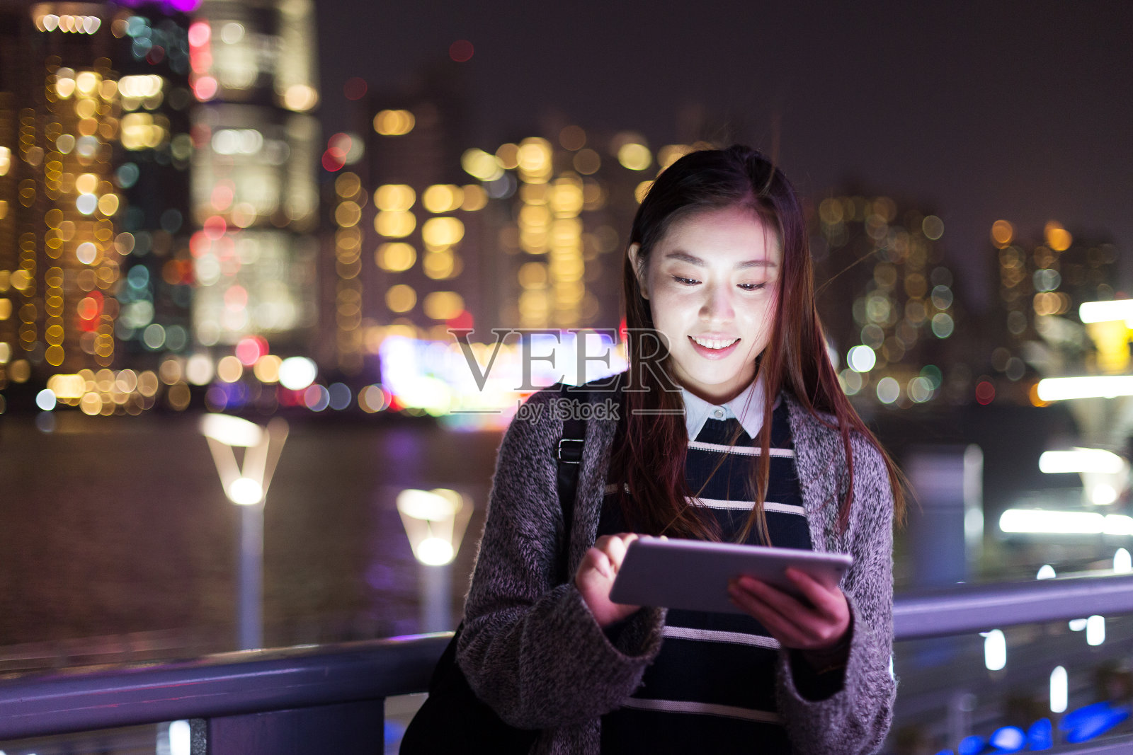 年轻美丽的亚洲女人晚上在现代城市玩数字平板电脑照片摄影图片