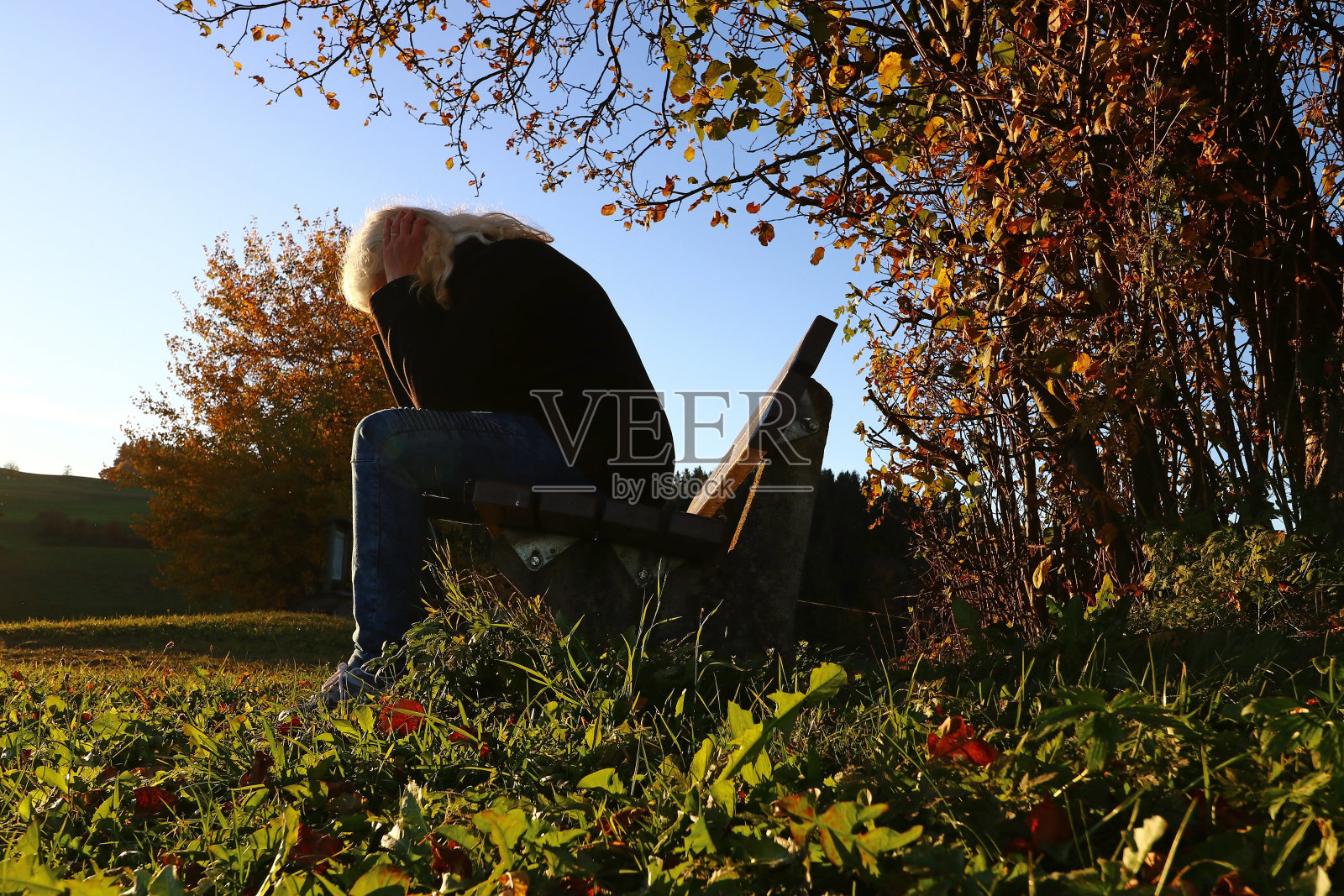 秋天的萧条。一个女人愁眉苦脸地坐在长凳上照片摄影图片