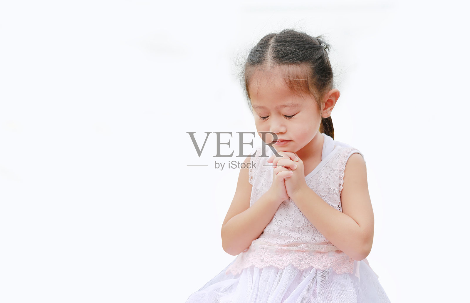闭上眼睛小亚洲女孩祈祷孤立在白色的背景。照片摄影图片