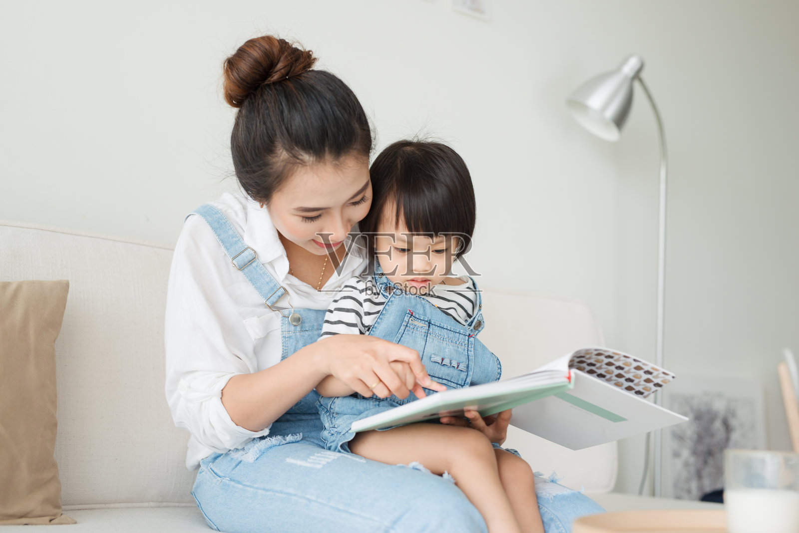 快乐幸福的家庭。年轻漂亮的亚洲母亲在给女儿读书照片摄影图片