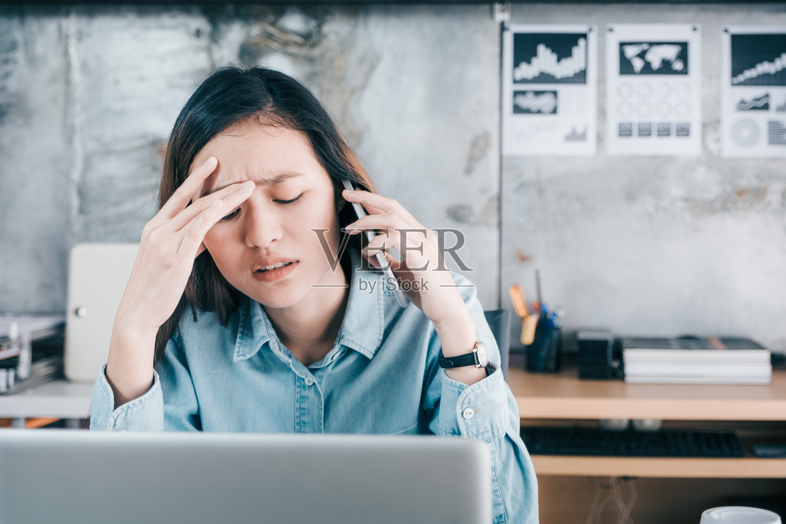 紧张的亚洲创意女设计师用手捂着脸，在办公室桌上的笔记本电脑前与客户通电话时感到不安，压力办公室的生活方式概念照片摄影图片