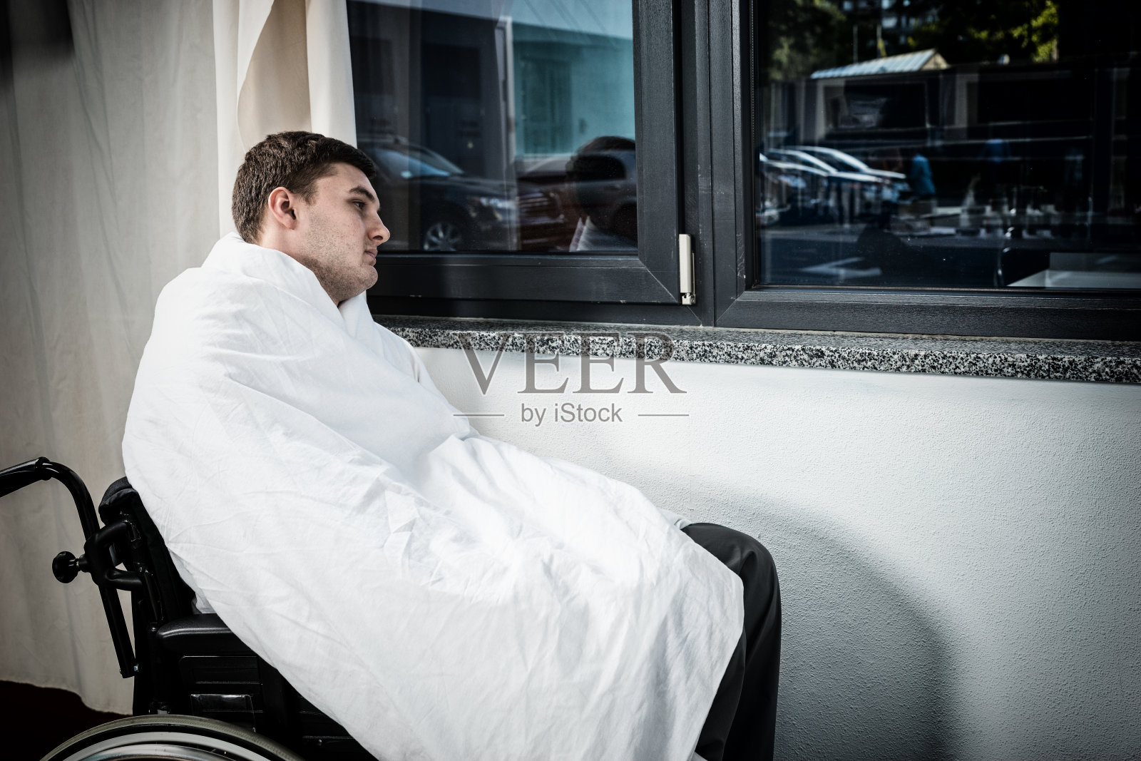 病房里一个悲伤的男病人，坐在靠窗的轮椅上，盖着被子照片摄影图片