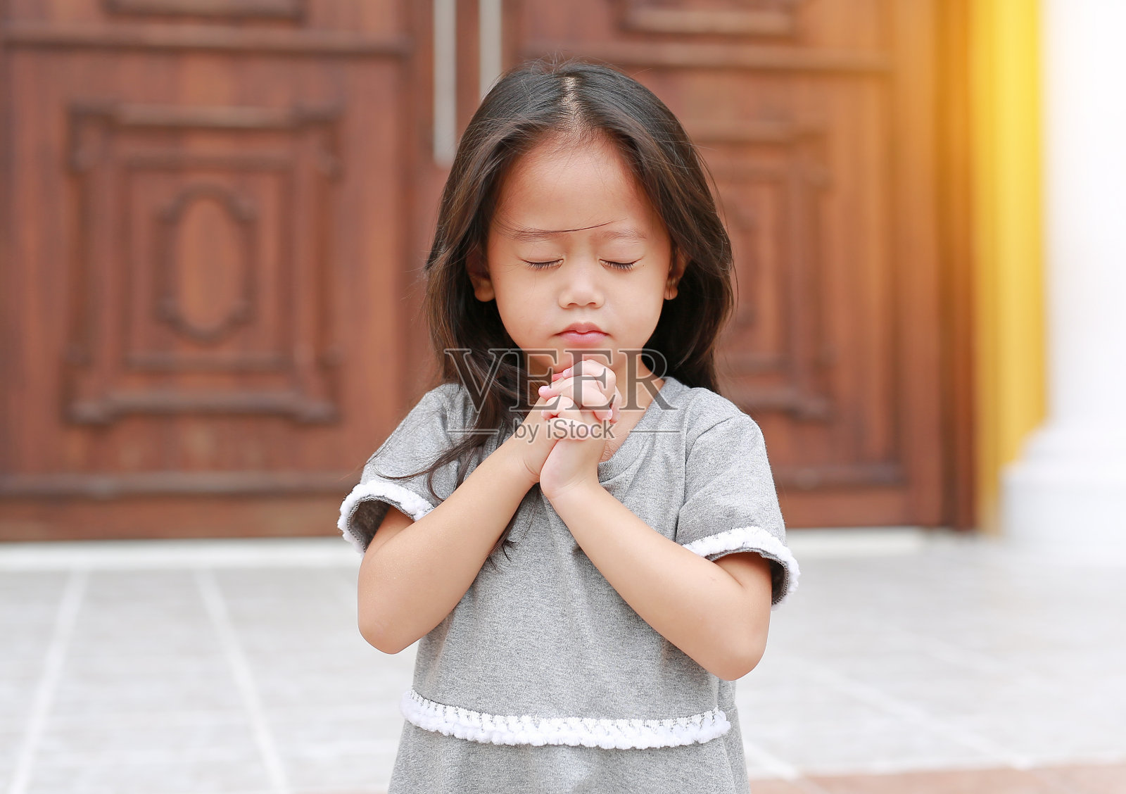 闭上眼睛，小亚洲女孩坐在教堂祈祷。照片摄影图片
