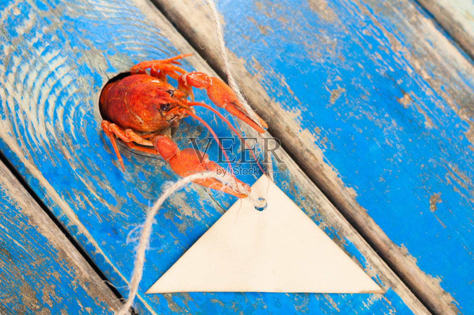 从一个洞里探出来的红煮小龙虾，带着空的棕色纸，三角形和绳子，放在古老的乡村蓝色木板上照片摄影图片