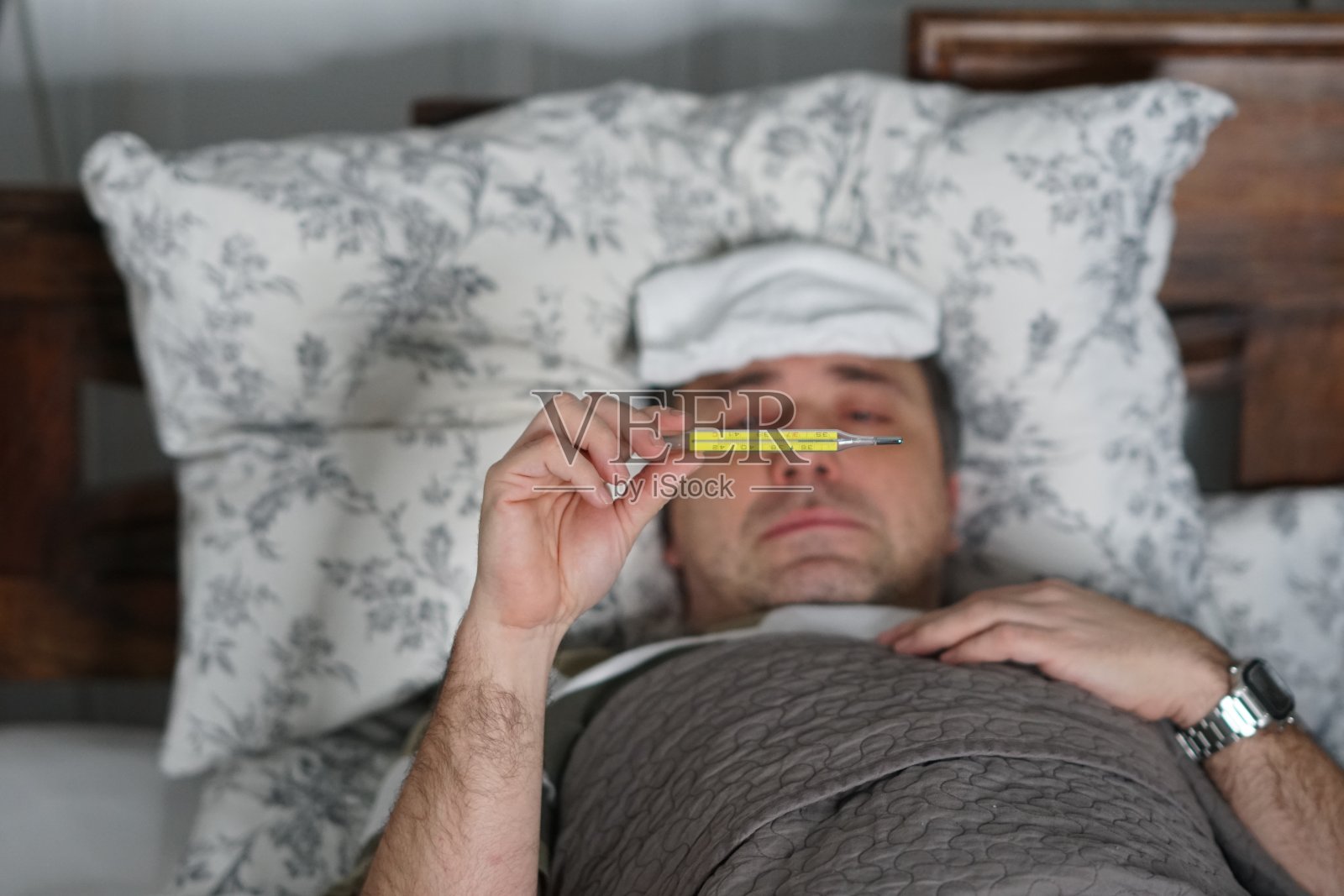 一个又累又病的男人躺在床上检查他的体温照片摄影图片