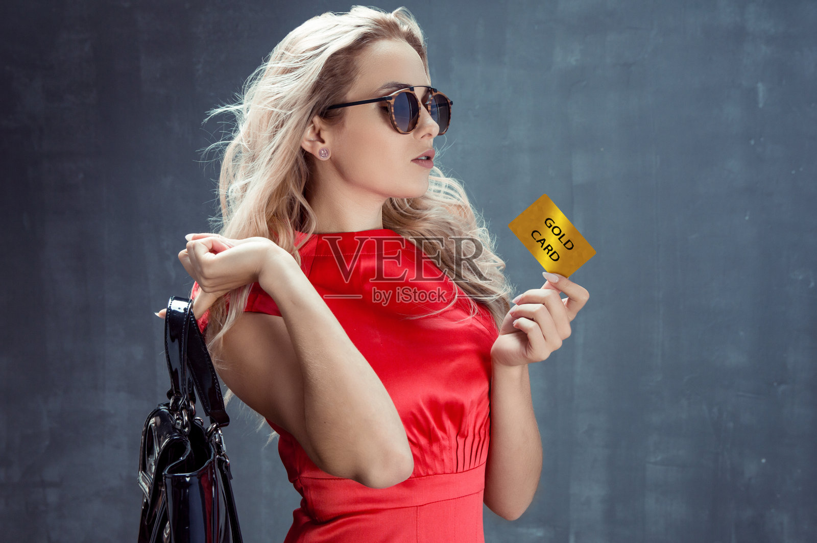 年轻优雅的金发女郎，肩上挎着包，手里拿着金卡照片摄影图片