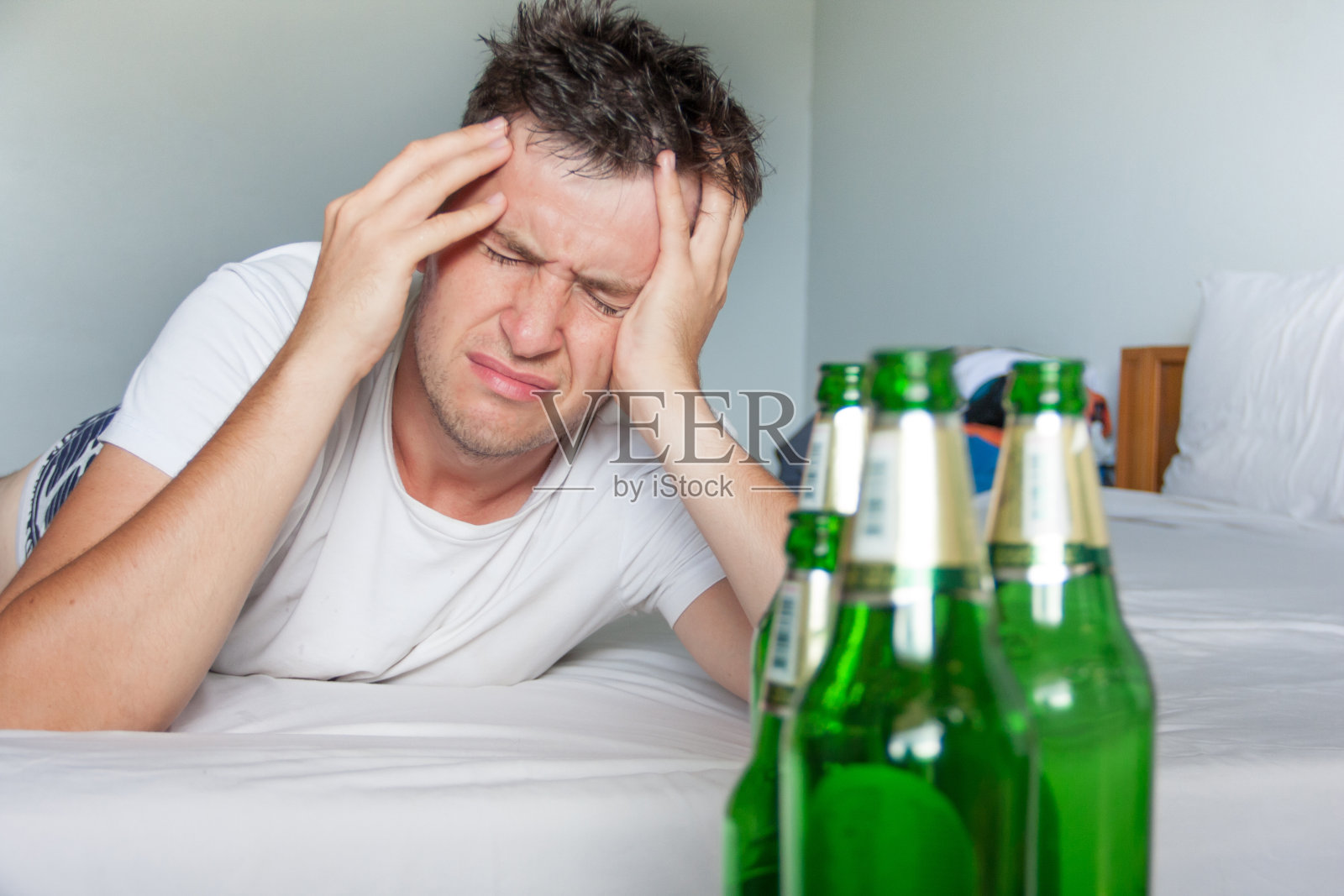 宿醉痛苦的男人近距离的肖像与啤酒瓶。照片摄影图片