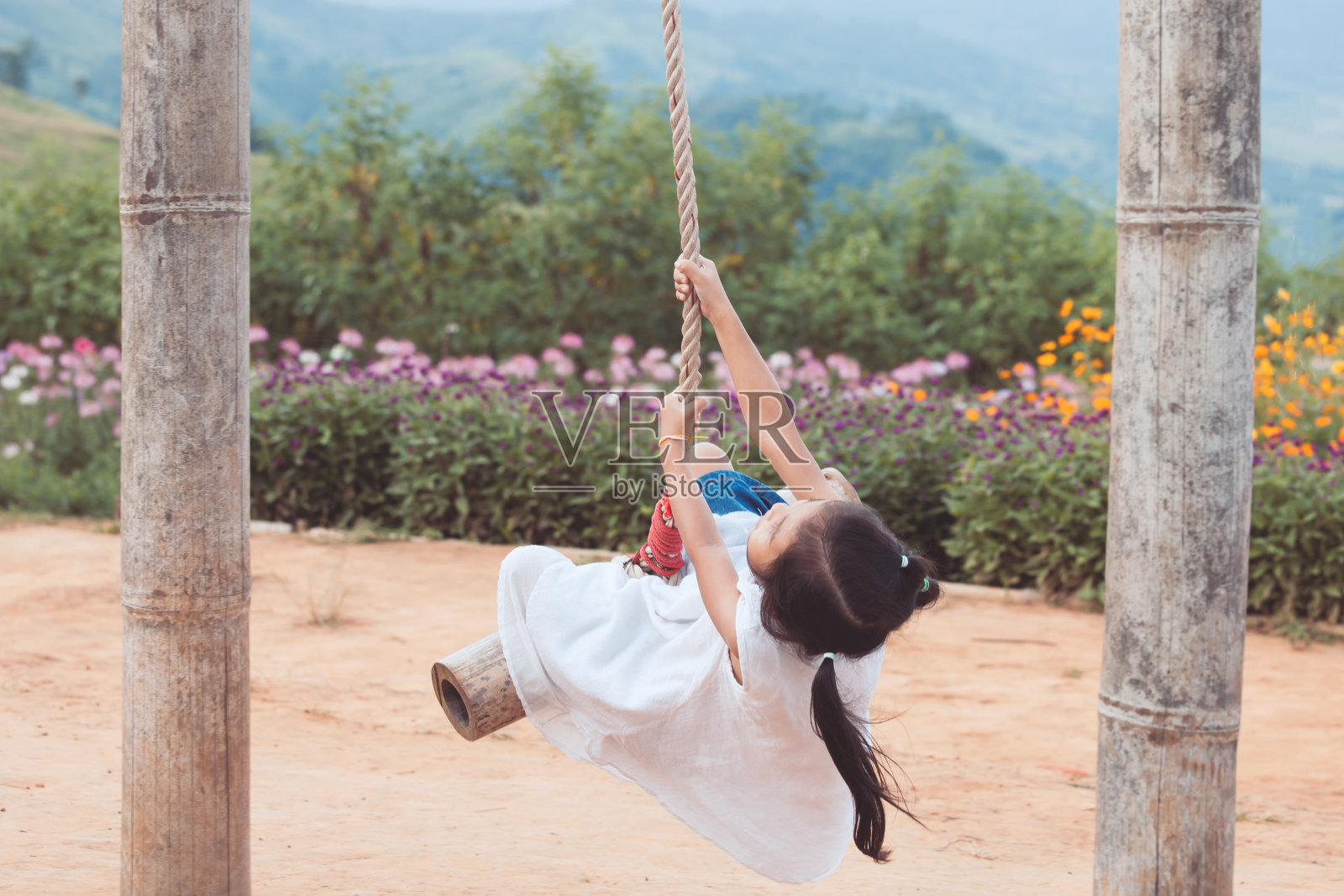 快乐的亚洲小女孩有乐趣在操场上玩木制秋千照片摄影图片