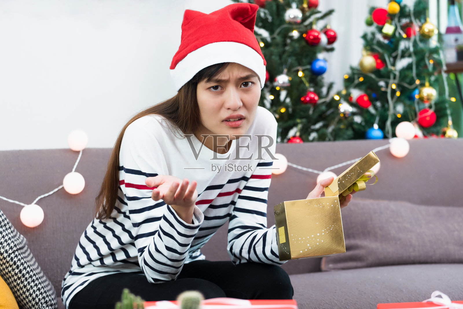 亚洲女人心烦意乱的时候在沙发上打开金色的圣诞礼盒，无聊的圣诞派对礼物。照片摄影图片