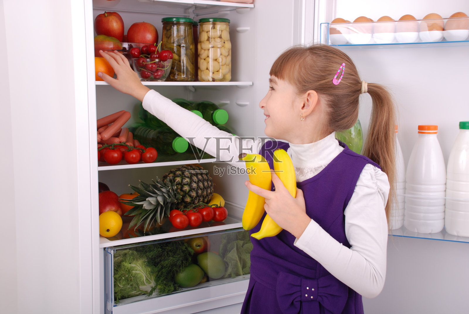 冰箱旁边有个漂亮女孩，吃着健康的食物。照片摄影图片