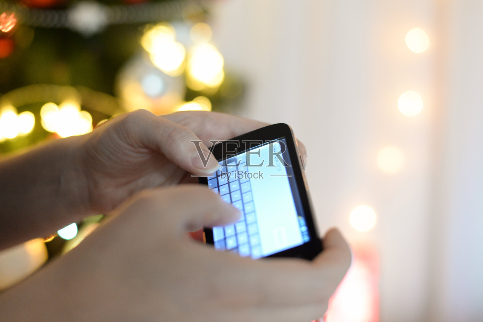 一名女子在圣诞树下发短信问候新年。照片摄影图片