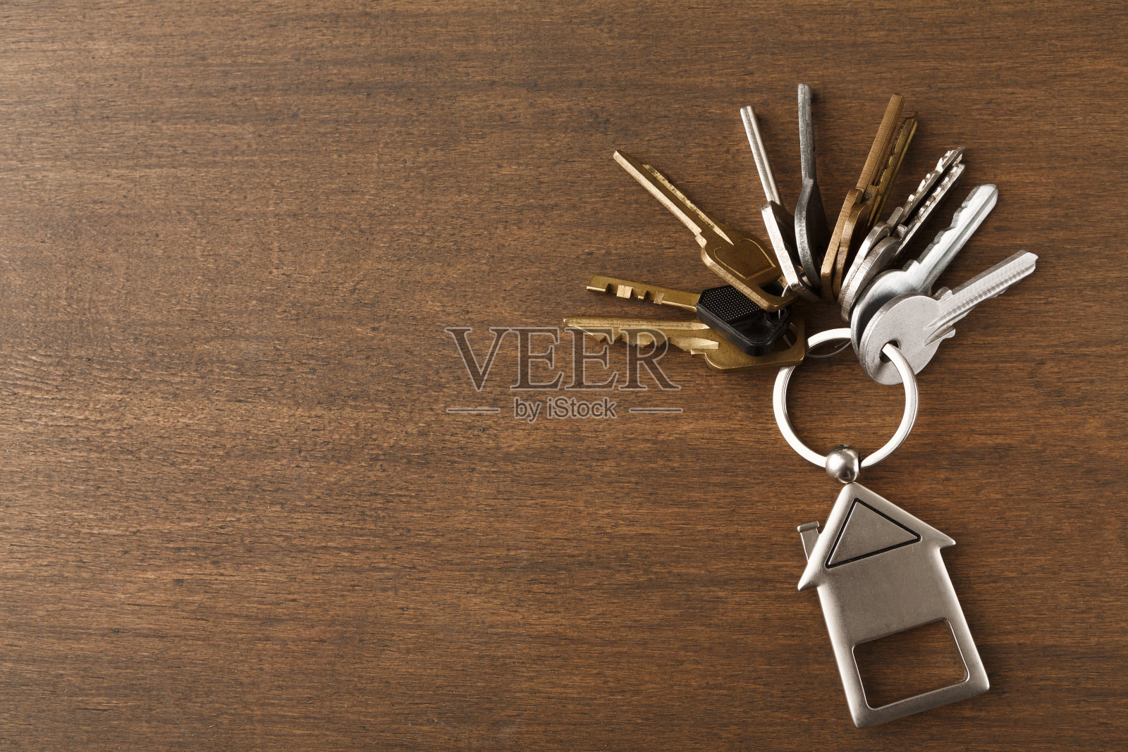 一串钥匙和房子形状的钥匙链在白色木头上照片摄影图片
