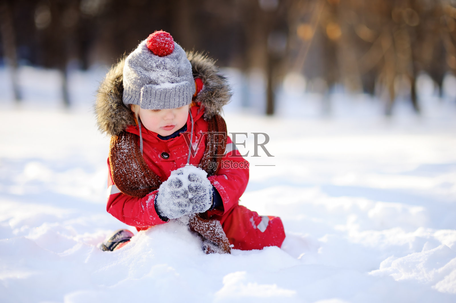 小男孩穿着红色的冬装和雪玩照片摄影图片