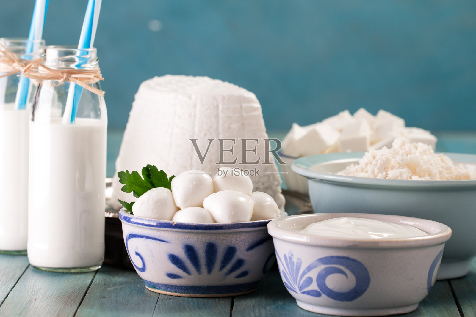 蓝色背景的桌子上放着美味健康的乳制品:酸奶油、白软干酪、马苏里拉奶酪、黄油、乳清干酪和一瓶牛奶照片摄影图片