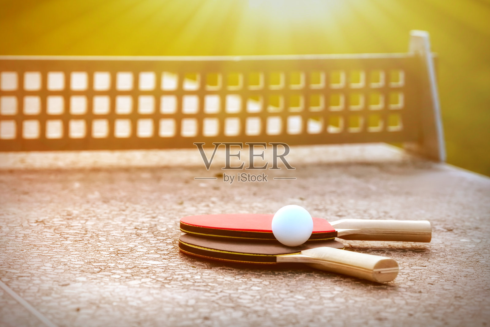在阳光下的石头网球桌上的乒乓球和网球拍的特写，户外乒乓球设备。户外运动的概念。健康的生活方式和物体概念照片摄影图片