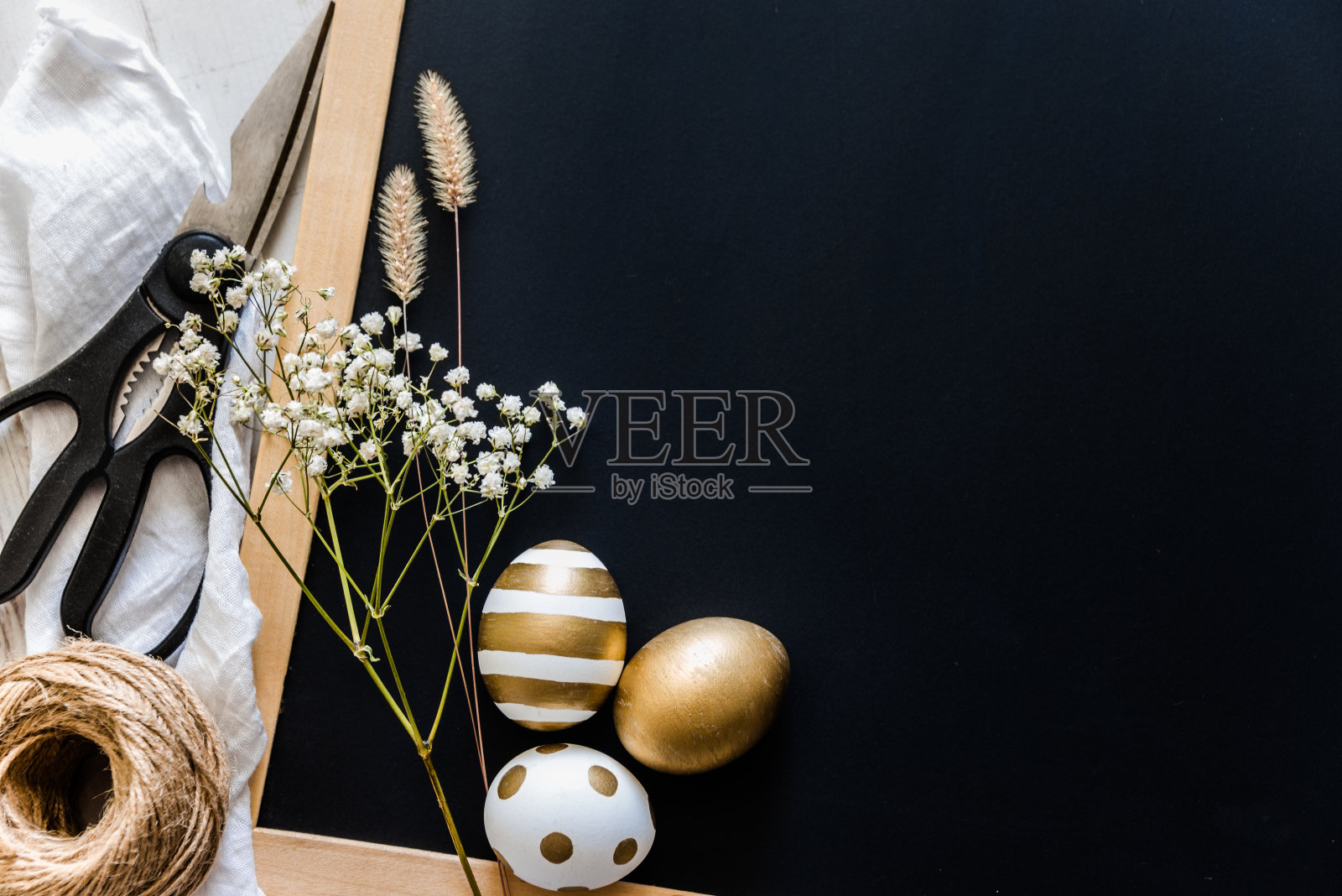 复活节的背景。复活节彩蛋在各种金色的设计，剪刀，花和麻球在黑色的故事板。副本的空间。照片摄影图片